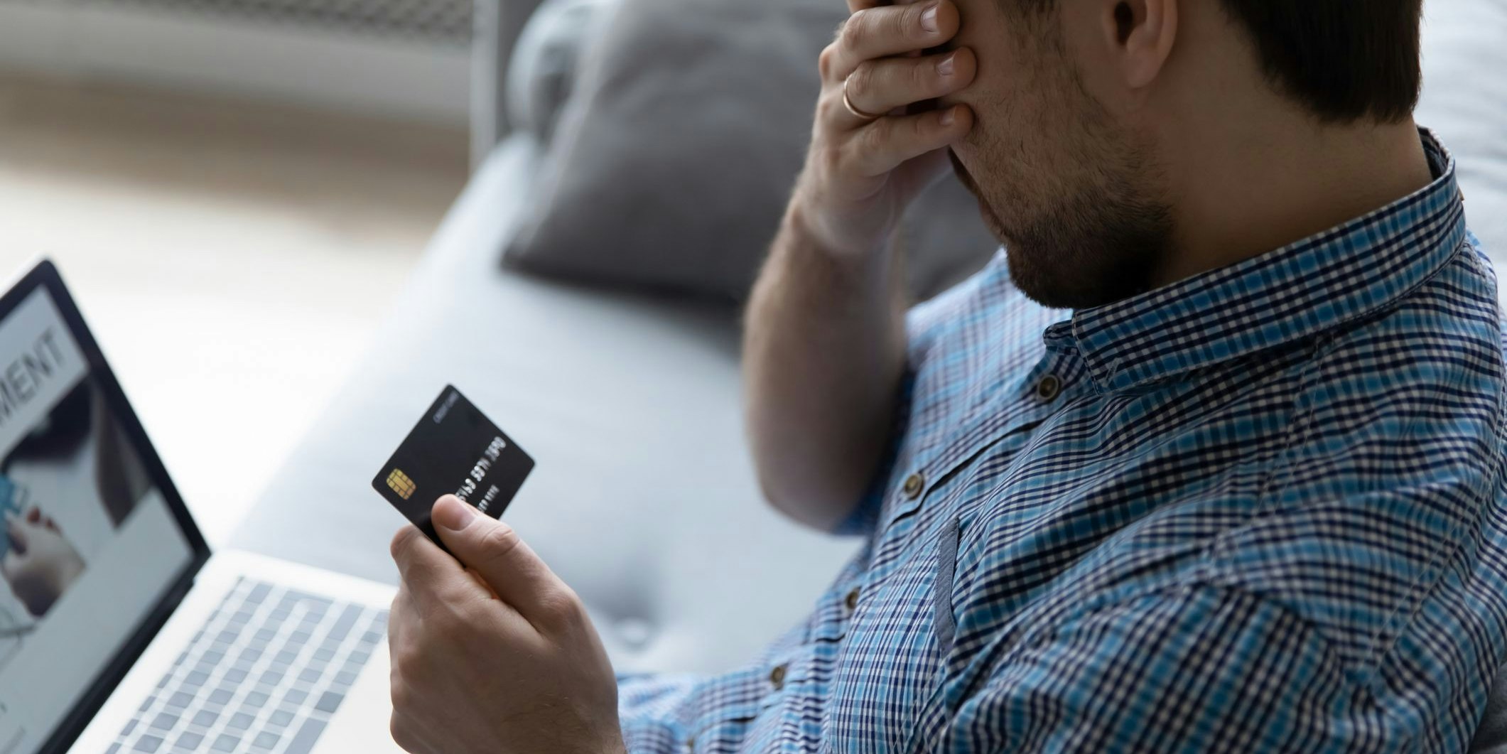 Close up unhappy man having problem with credit card, using laptop at home, depressed frustrated young customer client covering face with hand, loss money, cyber internet fraud and scam concept