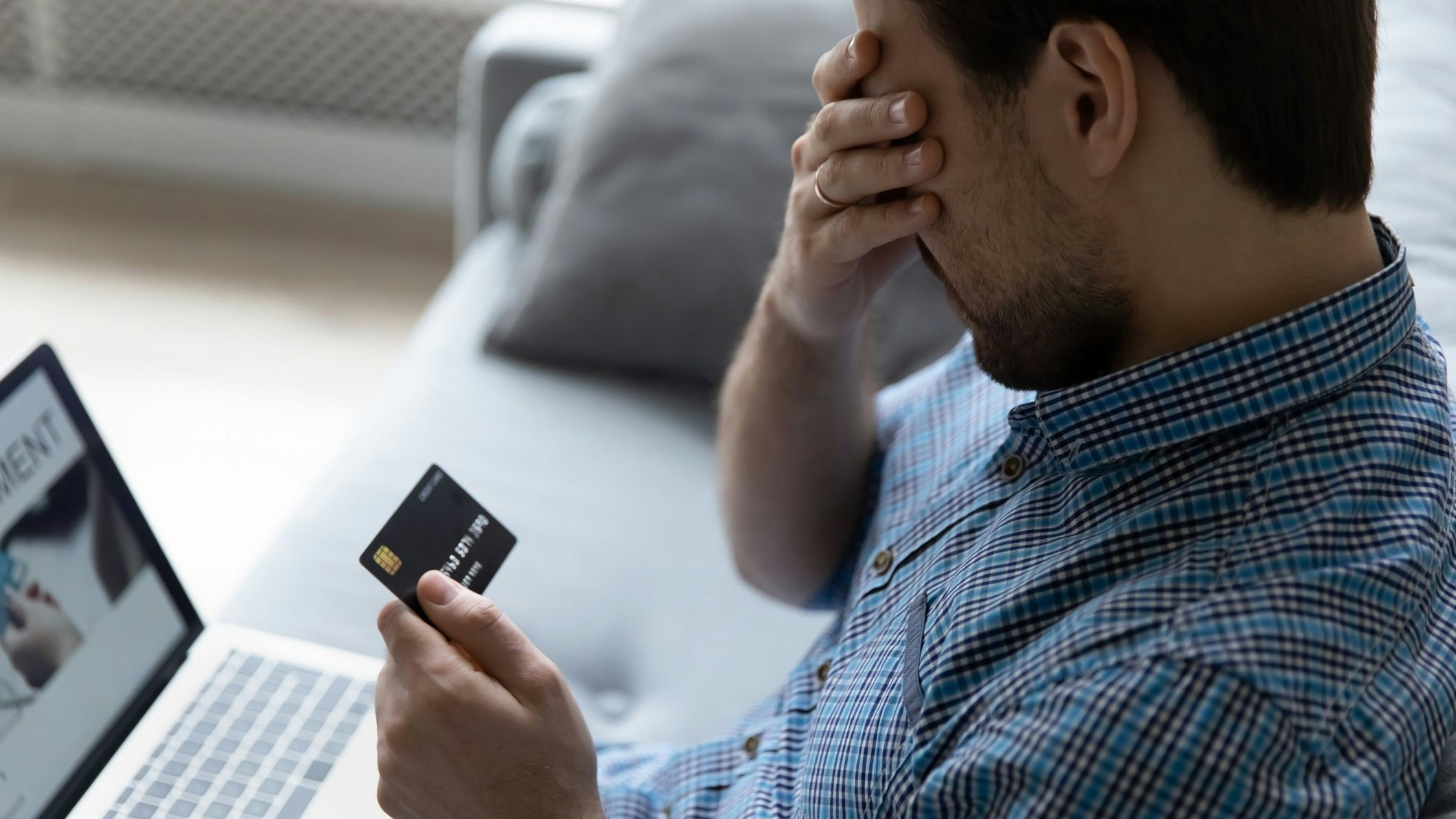 Close up unhappy man having problem with credit card, using laptop at home, depressed frustrated young customer client covering face with hand, loss money, cyber internet fraud and scam concept