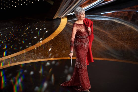 Jane Fonda auf der Bühne bei den Oscars in einem Traum in Rot. Lässig über die Schulter trägt sie ihr Cape.