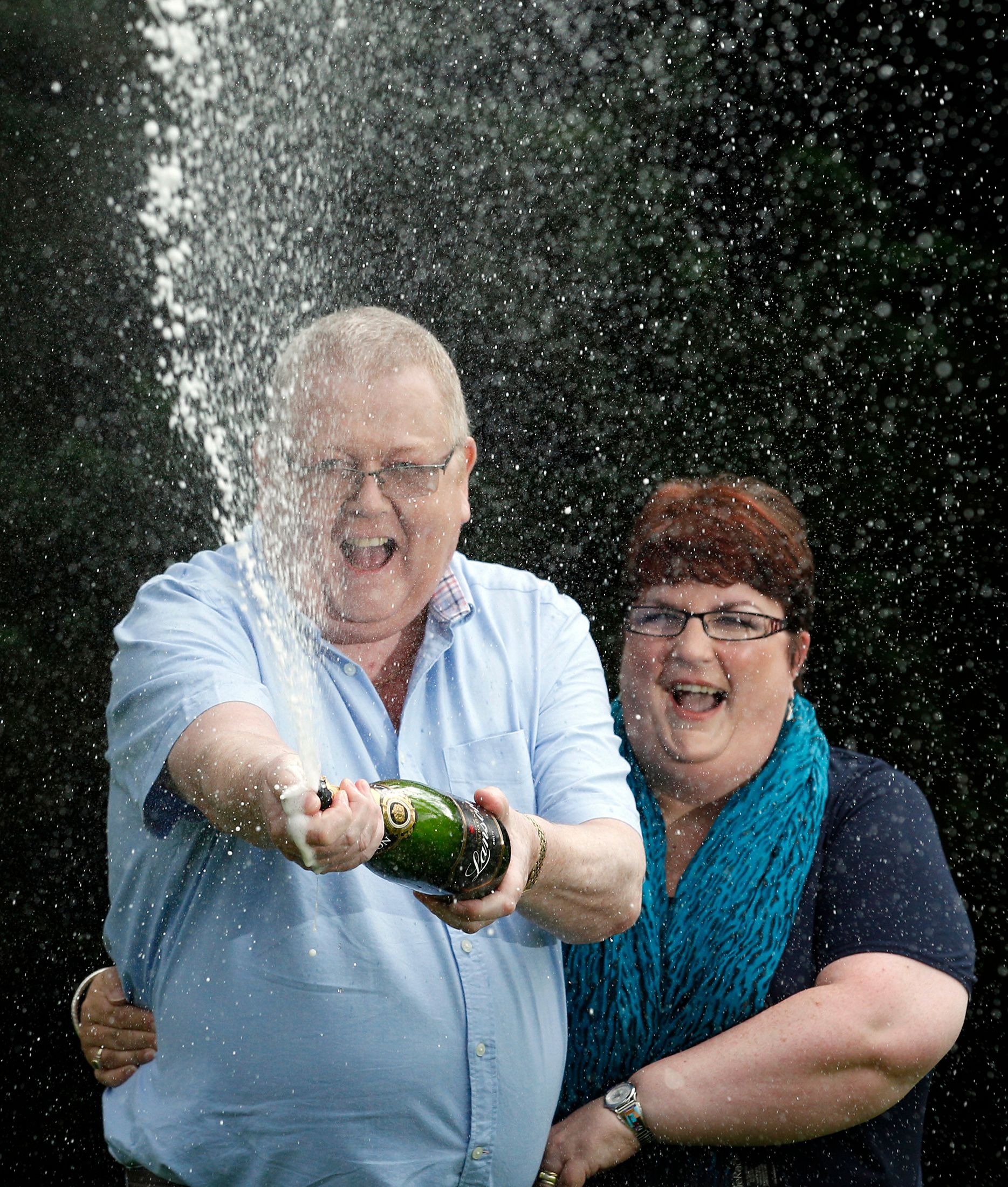 Colin Weir (L) and his wife Chris spray a bottle of champagne after a news conference at a hotel near Falkirk, Scotland July 15, 2011. The couple scooped 161 million pounds ($259 million) in Tuesday's Euromillions jackpot.   REUTERS/David Moir (BRITAIN - Tags: SOCIETY)