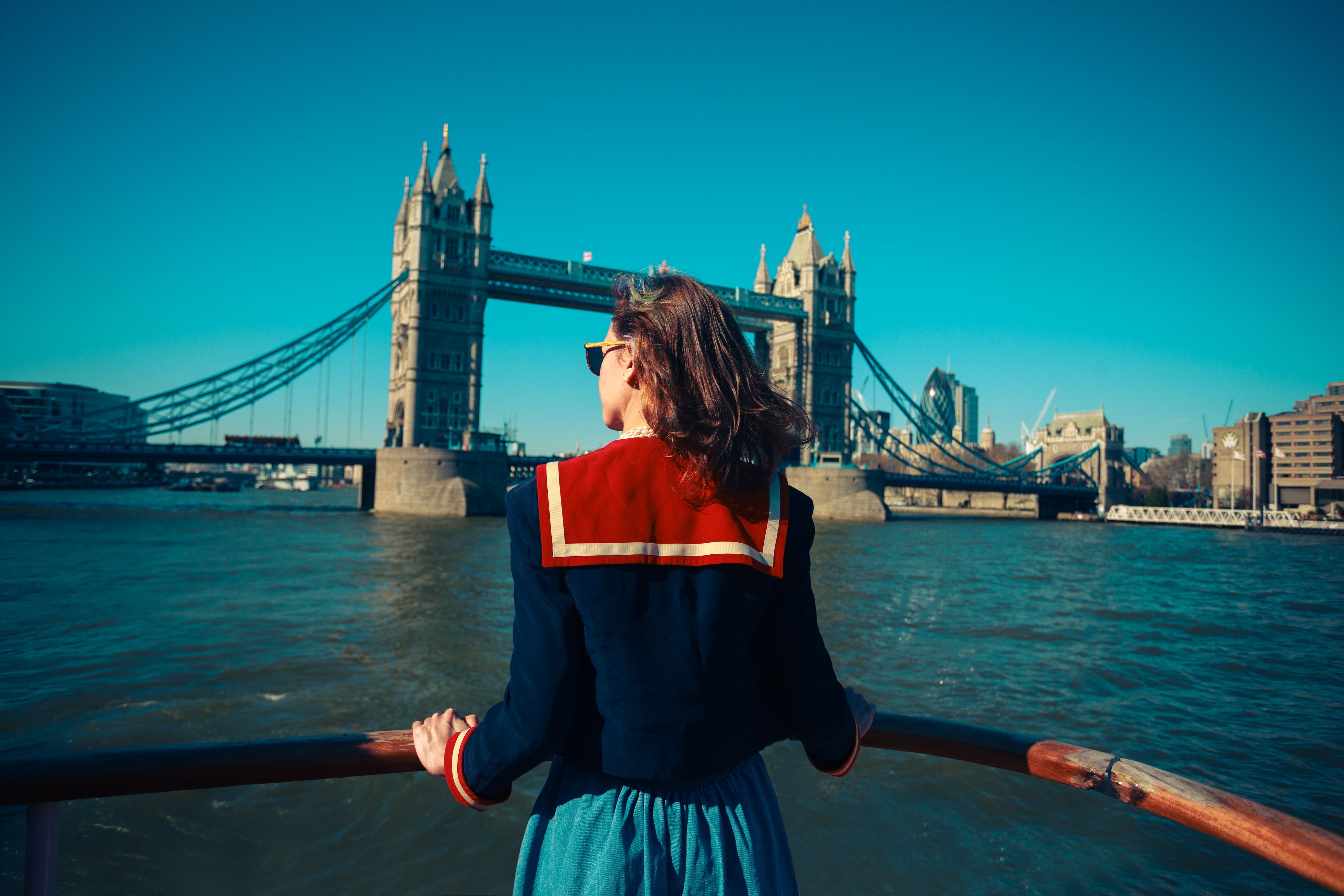 A young woman on a boat is looking at Tower bridge and the London skyline