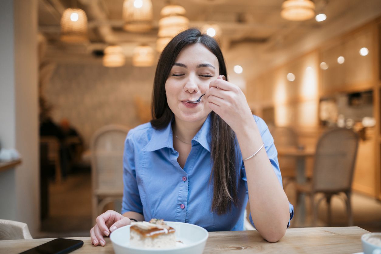 Happy young Caucasian woman enjoying herself in a coffee shop, satisfying her sweet tooth with a delicious cake