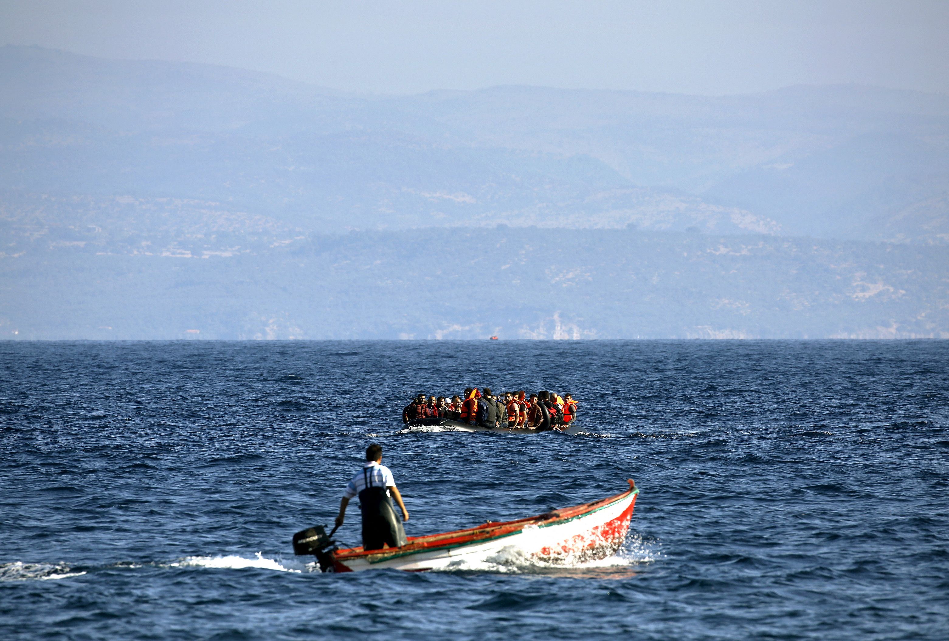 EDITORIAL USE ONLY - NO COMMERCIAL OR BOOK SALES. A Greek fisherman powers his boat, as a dinghy overcrowded with Syrian refugees approaches the Greek island of Lesbos while crossing a part of the Aegean sea from Turkey, September 17, 2015. REUTERS/Yannis Behrakis