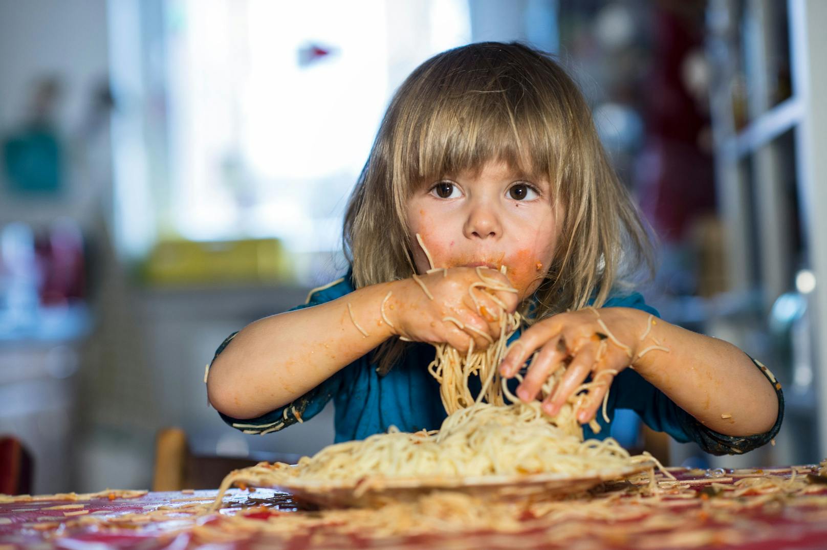 Long-haired Boy eating Spaghetti with his Hands.