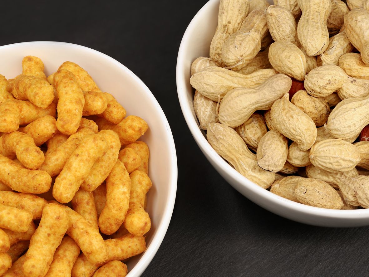 Portion of peanut flips and naturally roasted inshell peanuts in white bowls on black background, snack comparison of peanuts.