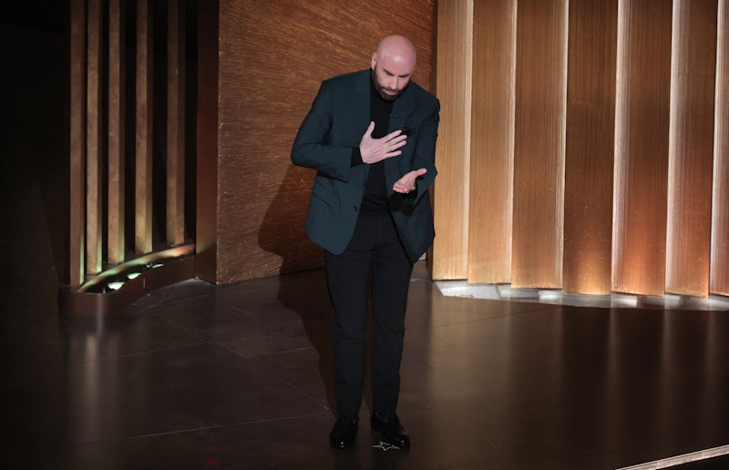 John Travolta hält eine Rede und ist den Tränen nahe, als er über verstorbene Mitglieder der Filmbranche spricht. 
