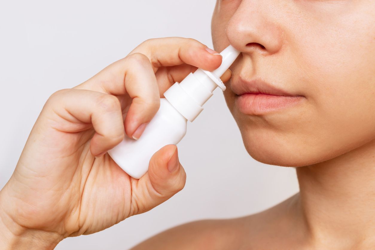 Cropped shot of a young caucasian woman using nasal spray for a runny nose and congestion isolated on a white background. Treatment of the disease. Rhinitis, sinusitis, cold. Dependence on drops