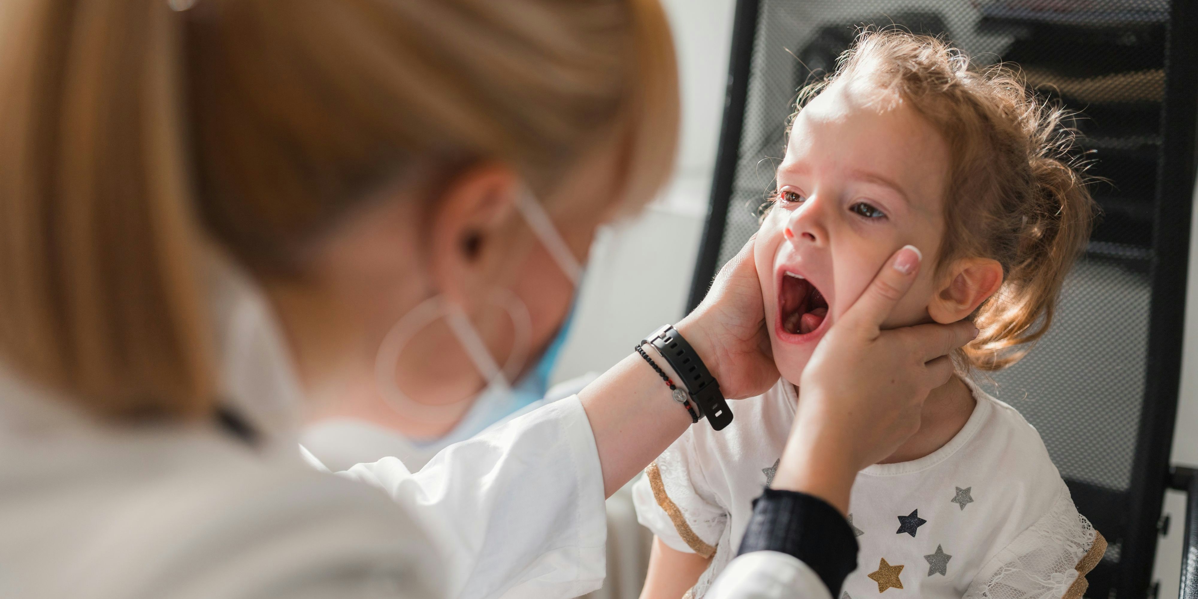 Female doctor wearing a protective mask when checking young girl tonsils before vaccinating her for Covid-19 disease