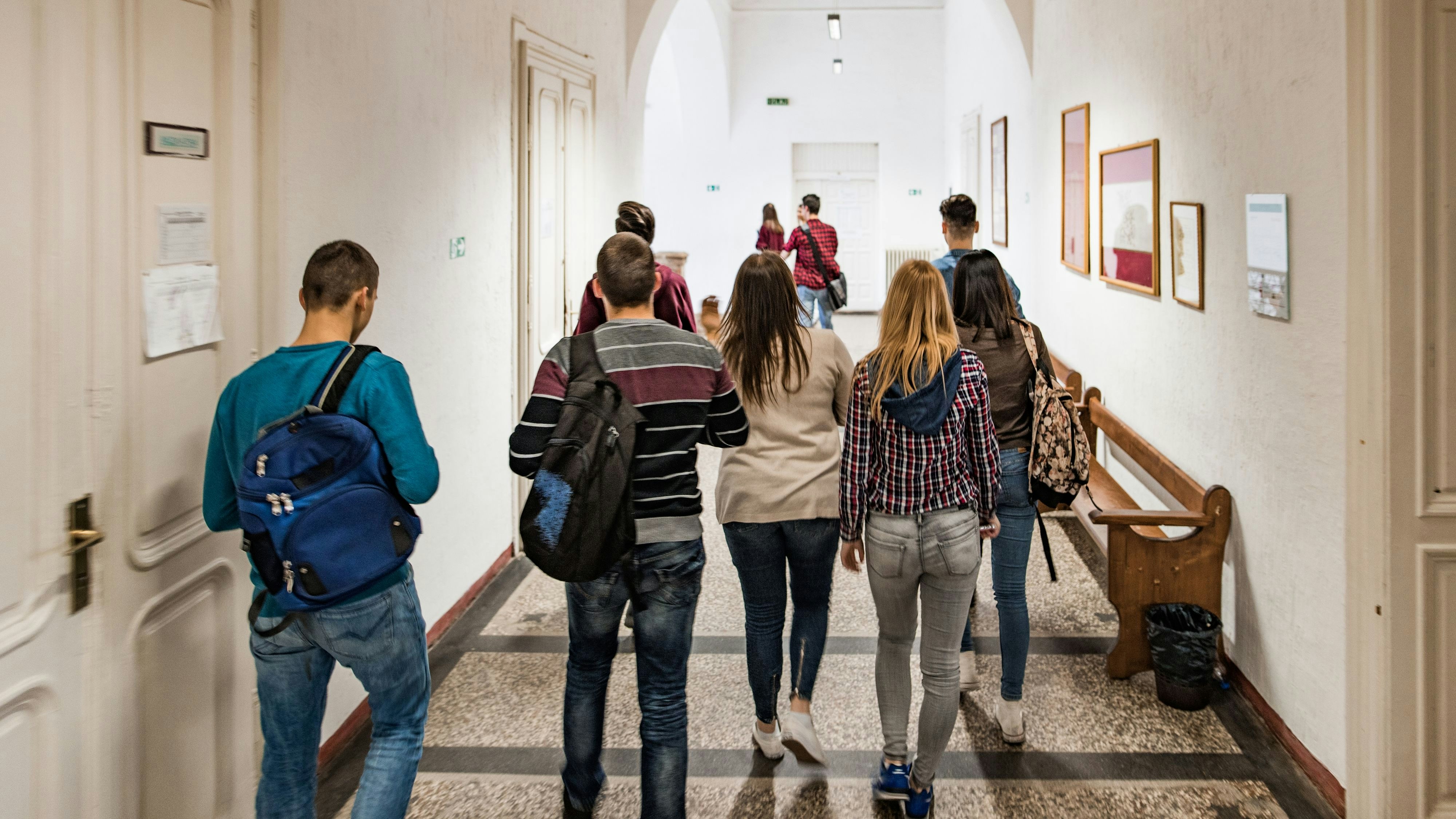 Rear view of high school students walking in the school hallway.