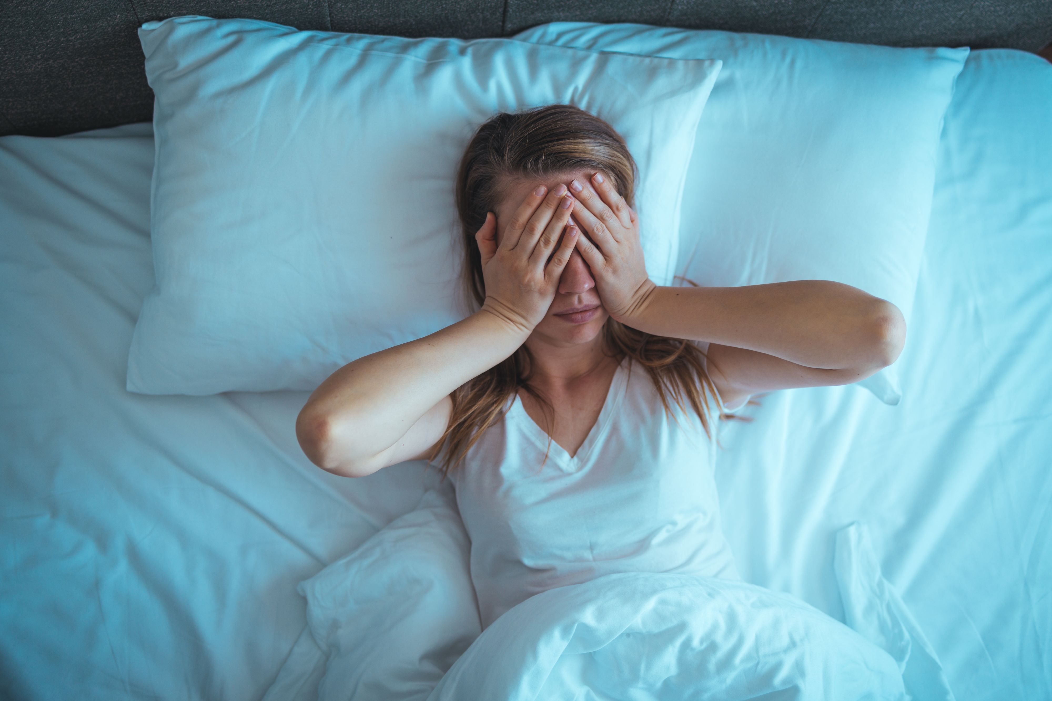 Young stressed woman lying on bed late at night suffering from insomnia, sleep apnea or stress. Top view of depressed girl lying bed. High angle view of awake girl in the middle of the night.