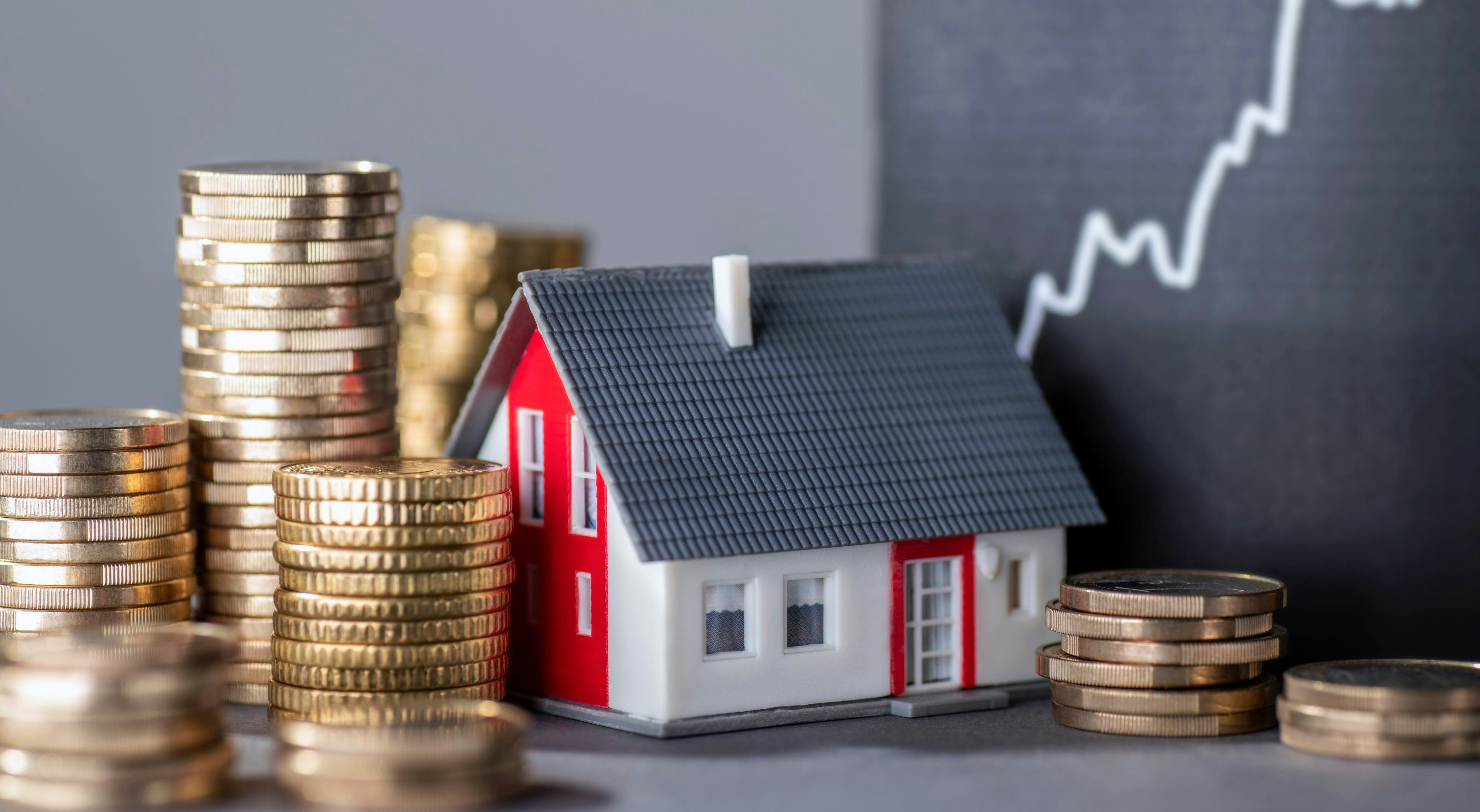 House with stacks of money and a rising curve symbolizing rising real estate prices