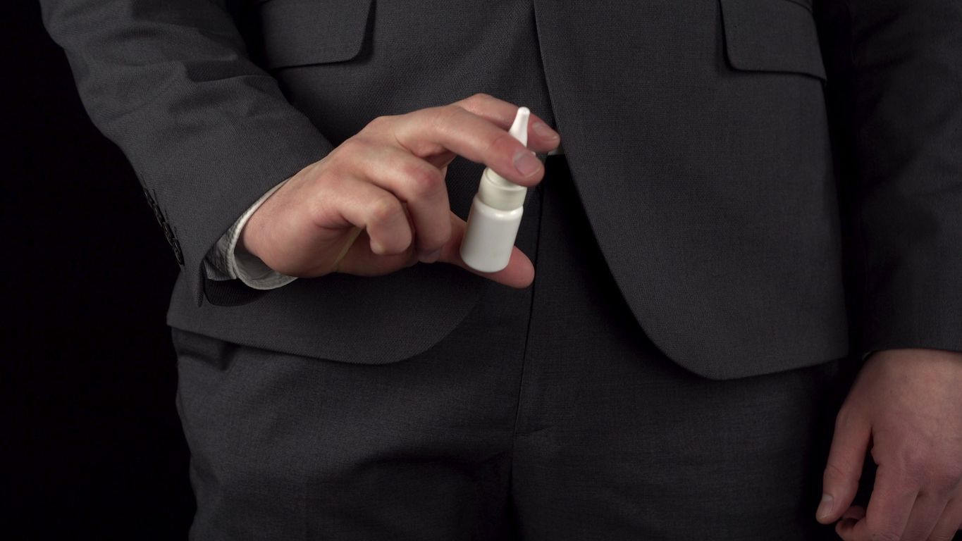 A young businessman in a suit pulls out a nasal spray from his pocket and sprays it into his nose. The waist of a man close-up on a black background. 4k