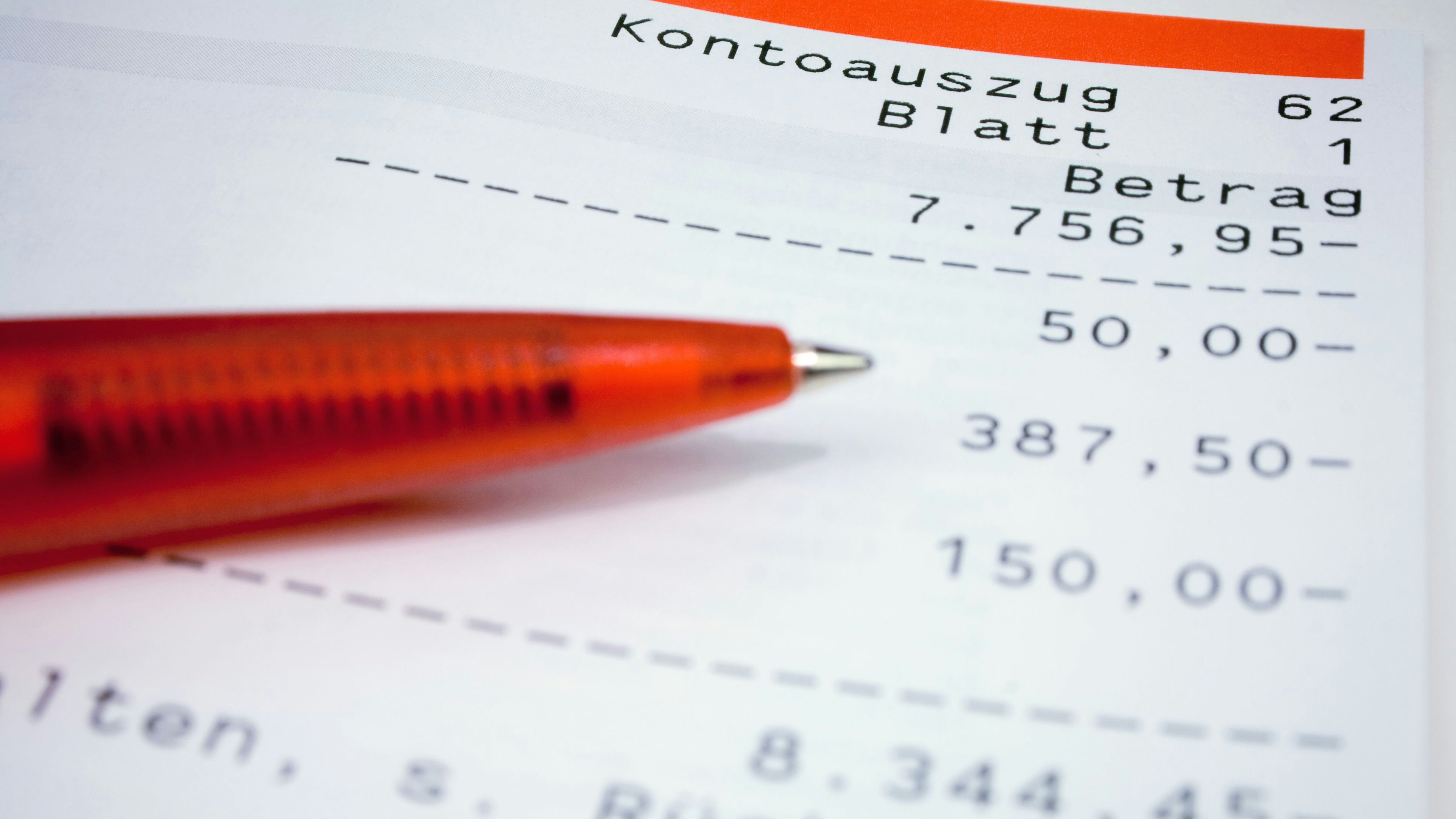 Statement of an bank account which slides further into minus. Part of red ball pen. German language.