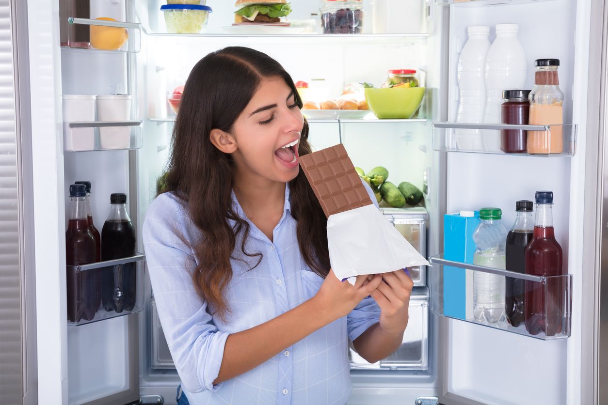 Young Woman Enjoying Chocolate In Front Of Refrigerator
