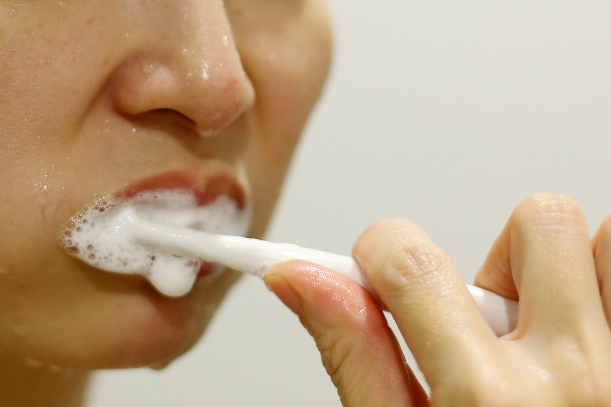 An Asian woman is enjoying brushing teeth after shower in bathroom.