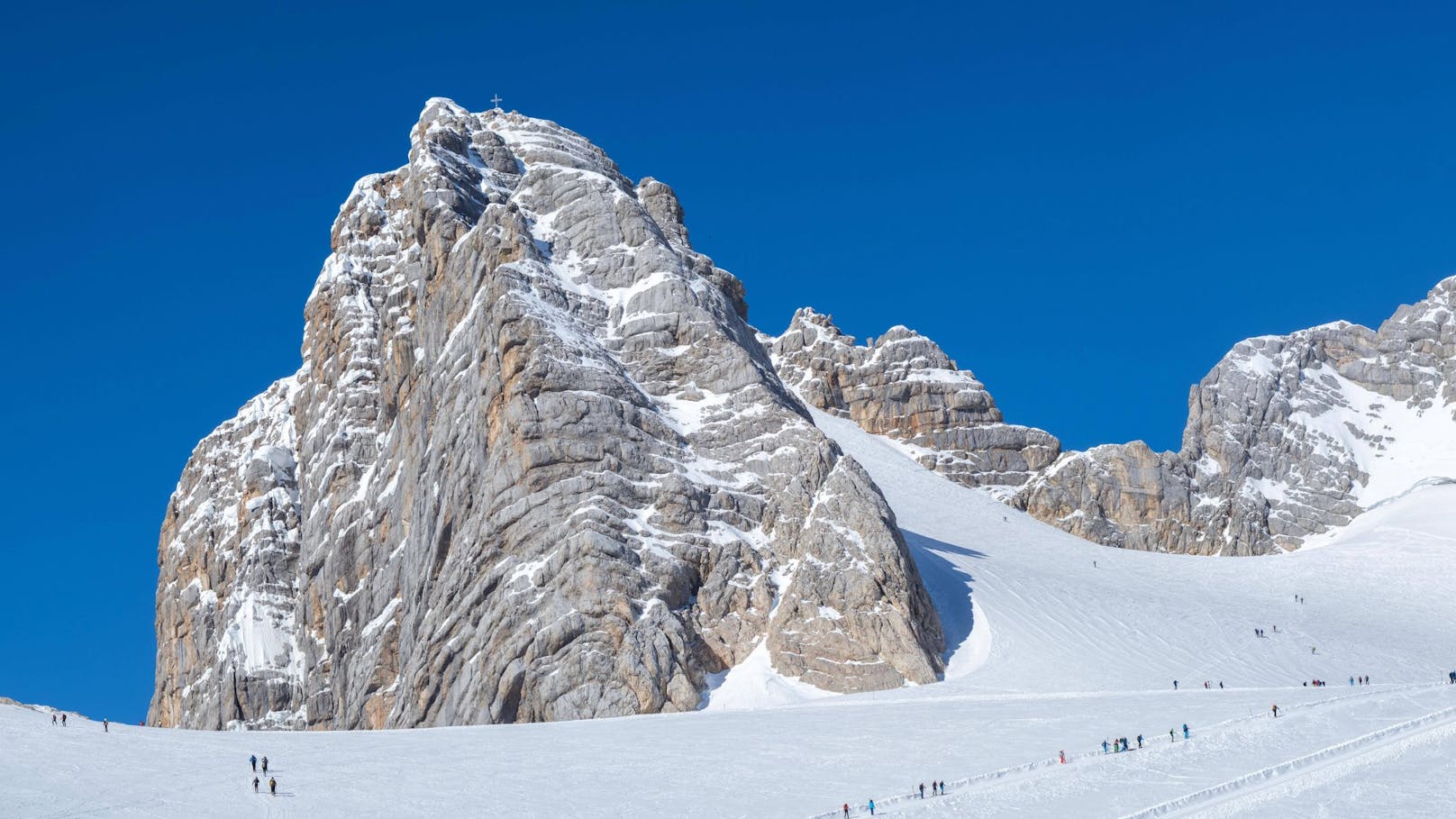 Skitourengeher auf dem Weg zum Hohen Dachstein mit Gipfelkreuz. Der Dachstein ist der höchste Berg der Steiermark.