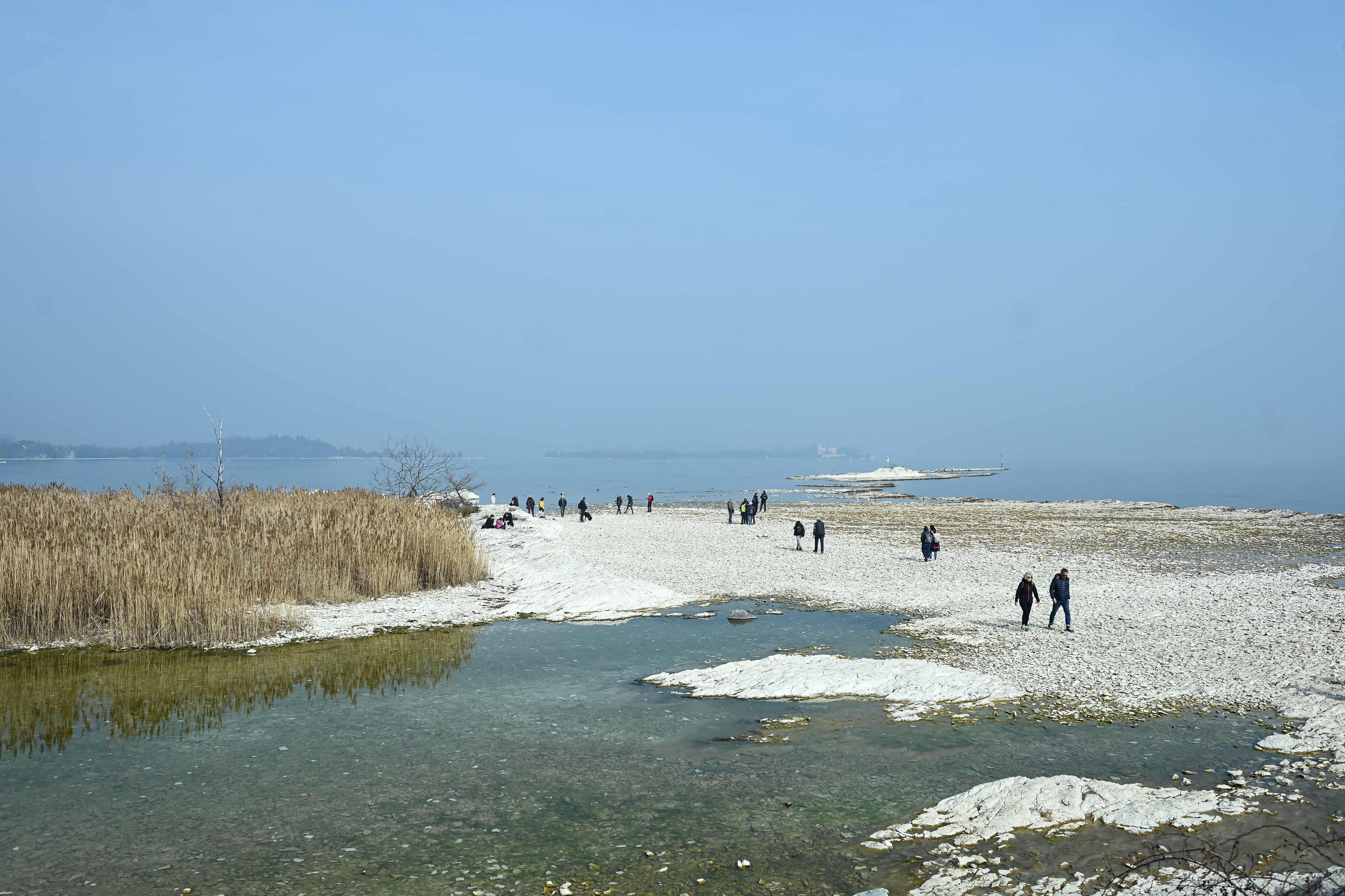 Download von www.picturedesk.com am 17.04.2023 (08:09).  People walk on the small island of San Biagio, off Manerba del Garda, Lake Garda, on February 21, 2023, where the water level dropped to its lowest in 30 years during the winter months. - A lack of snow on the surrounding mountain peaks, the absence of rain for the past six weeks, and mild temperatures - this explosive cocktail has caused the water level of Italy's largest lake to drop to its lowest in 30 years during the winter months. (Photo by Piero CRUCIATTI / AFP) - 20230221_PD16132 - Rechteinfo: Rights Managed (RM) Nur für redaktionelle Nutzung! Werbliche Nutzung erfordert Freigabe: bitte schicken Sie uns eine Anfrage.