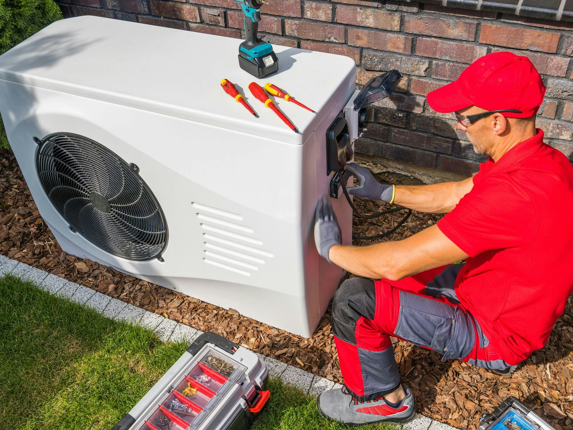 Professional Middle Aged HVAC Technician in Red Uniform Repairing Modern Heat Pump Unit. House Heating and Cooling System Theme.