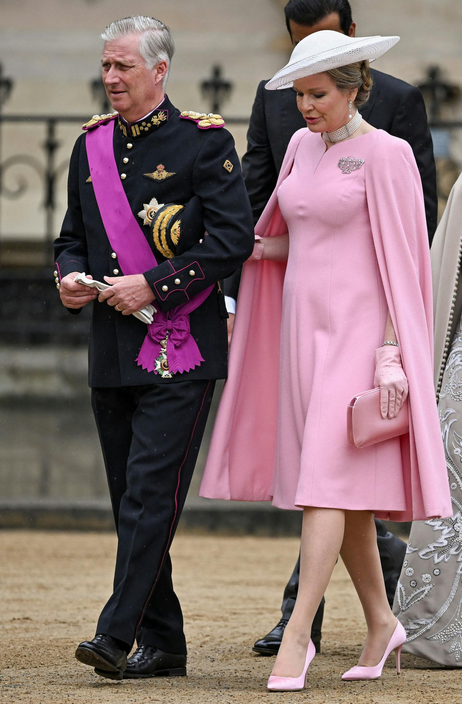 (König Philippe und) Königin Mathilde von Belgien kam in&nbsp;einem Cape-Kleid in Rosa. Ein Collier, Ohrringe, eine Brosche und ein Armband sorgen für Glitzer-Akzente.