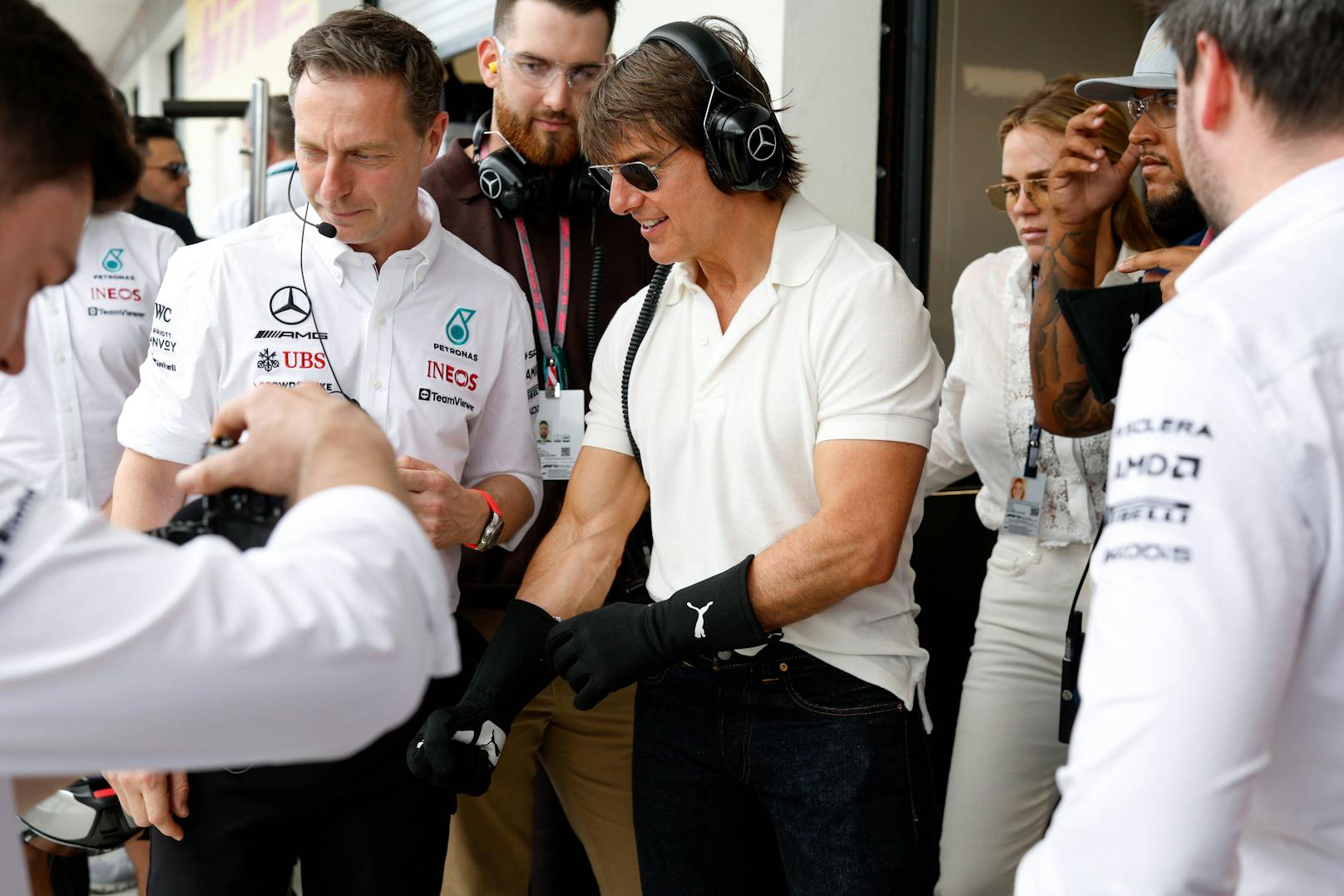 Tom Cruise (Mitte) darf in der Mercedes-Box die Handschuhe überstreifen und sich im Reifenwechseln versuchen.