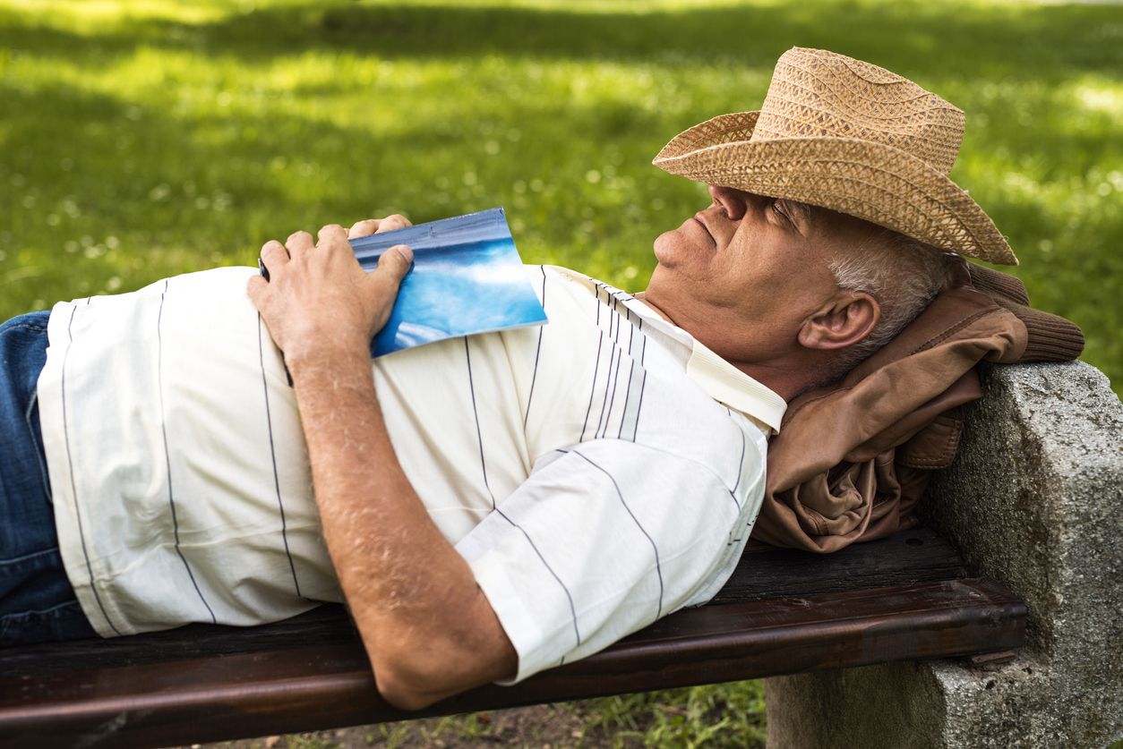 Old man resting on a bench at the park and sleeping with hat on his head.
