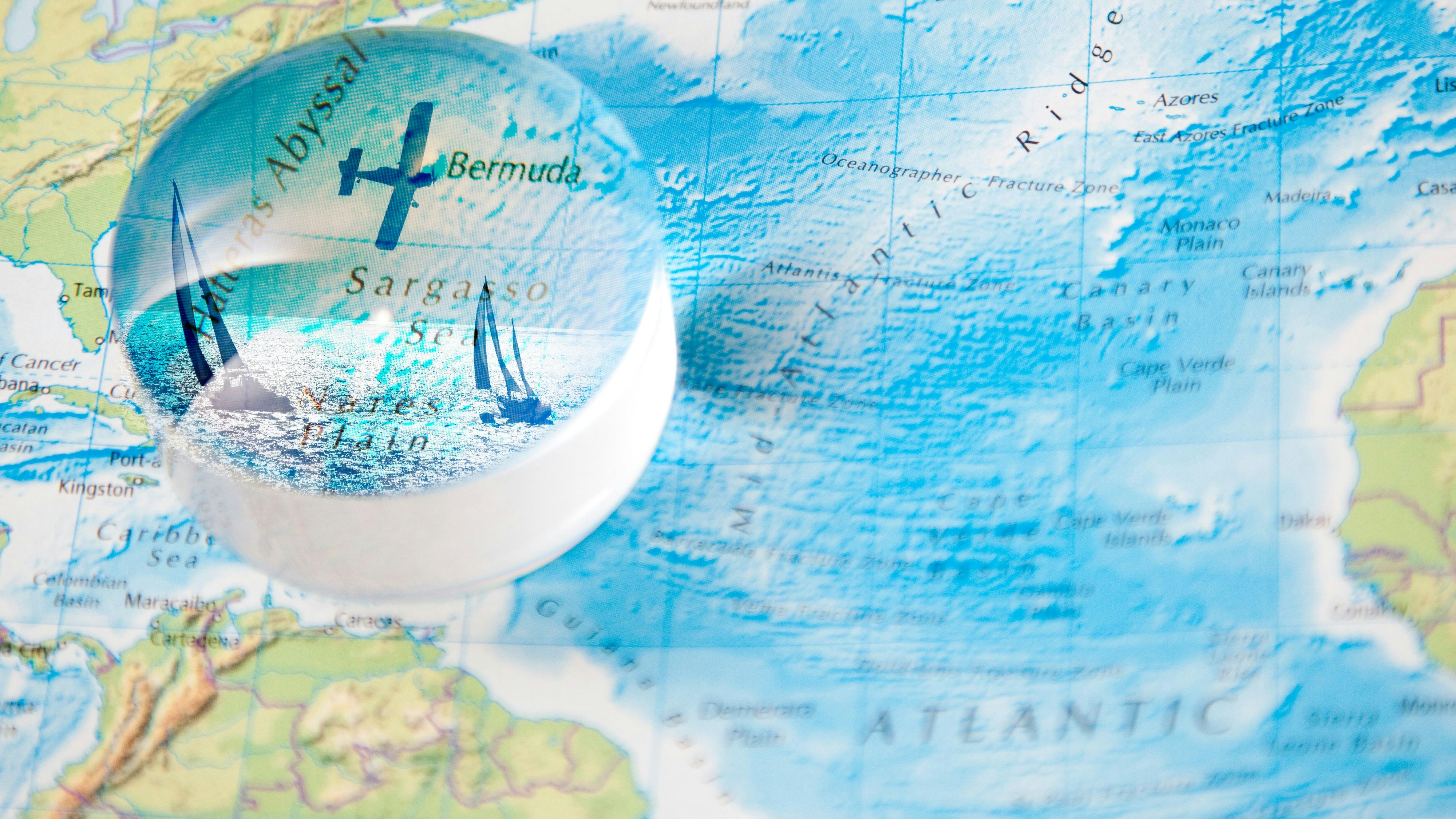 magnifying globe shows plane and boats over map of bermuda triangle