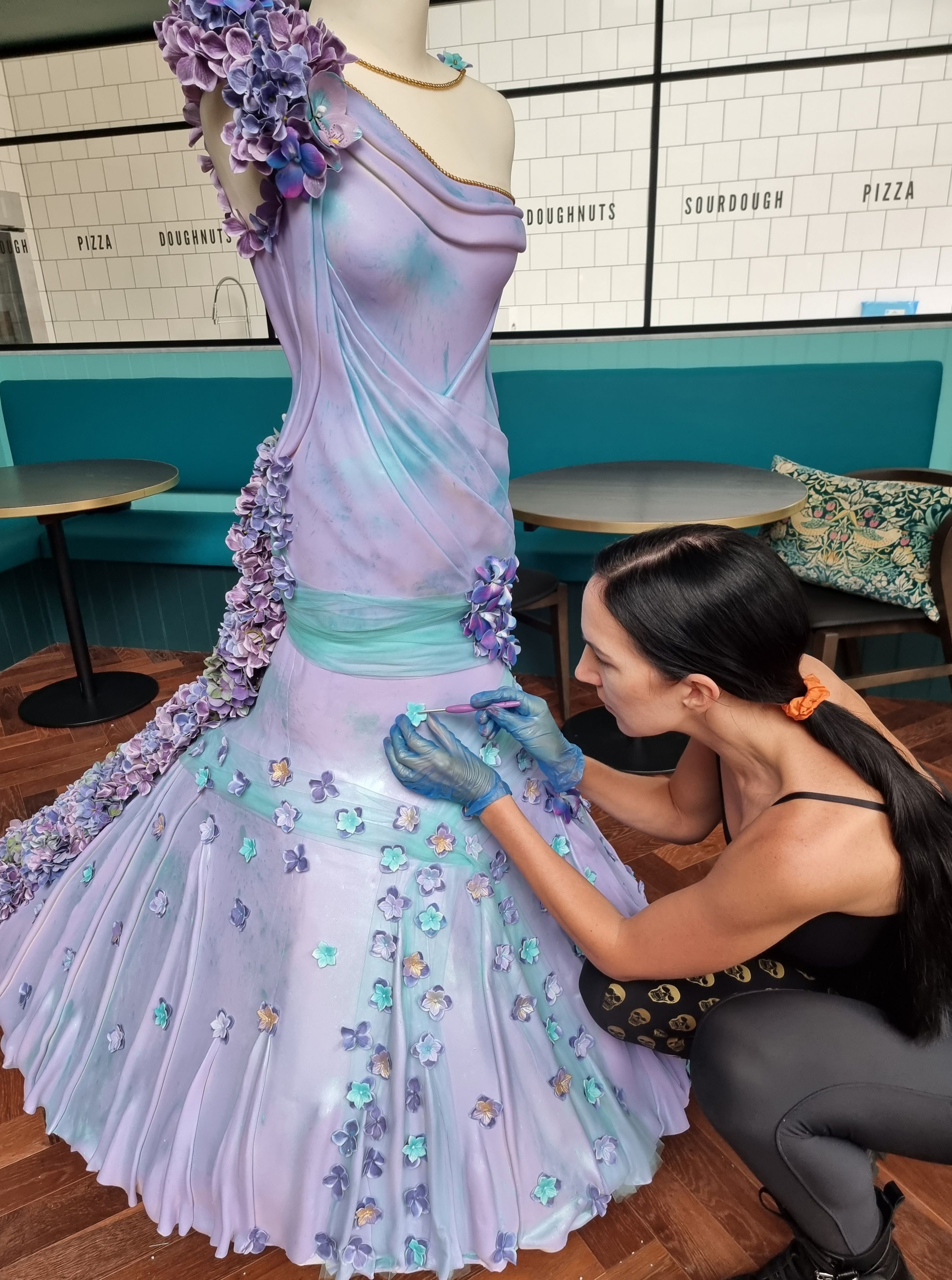 Download von www.picturedesk.com am 22.05.2023 (19:46).  May 17, 2023, London, United Kingdom: A renowned designer has created a dress made out of cake featuring a record breaking 25,000 edible flowers. Debbie Wingham has been called the Countess of Confection by Food Network thanks to her famous life-size cakes of celebrities, including Kim Kardashian, Karl Lagerfeld and Ru Paul. She even crafted a lavish a million-dollar wedding cake that was dripping in diamonds .And now Debbie is back in her apron and has curated an incredible life-size vintage inspired haute couture mannequin cake, adorned with an edible gown. The cake itself was created to mark the launch of Bread Aheads afternoon tea, which will be served in their new tearoom located above the Bread Ahead Boutique in the heart of Chelsea .Also inspired by The Chelsea Flower Show, which starts next week, the back of the dress is embellished with more than 25,000 edible flowers - the largest number of edible flowers ever featured on a cake .Every flower was cut individually with a flower press cutter and crafted from rice paper. It's no surprise that the complex design took Debbie months to craft. The flowers include hydrangeas, Phalaenopsis Orchids and Dendrobium Orchids created from petal paste .To create the huge cake, Debbie worked with ginormous amounts of ingredients. They included 300 eggs, 25 boxes of Rice Krispie treats, 29kg of couture sugar paste and 13,000 baby marshmallows. She also used almost half a ton of flour, which is around 1000 pounds. To put that into context, that's roughly the same weight as a small horse! The skirt of the dress is crafted from different flavour profiles from afternoon tea, such as creme mousseline and raspberry jam. The back of the gown contains the most edible flowers and also includes dark chocolate sponge with poached cherries and Chantilly cream. There's also a layer of chocolate ganache and an outer layer of suga - 20230517_PD11007 - Rechteinfo: Rights Managed (RM)