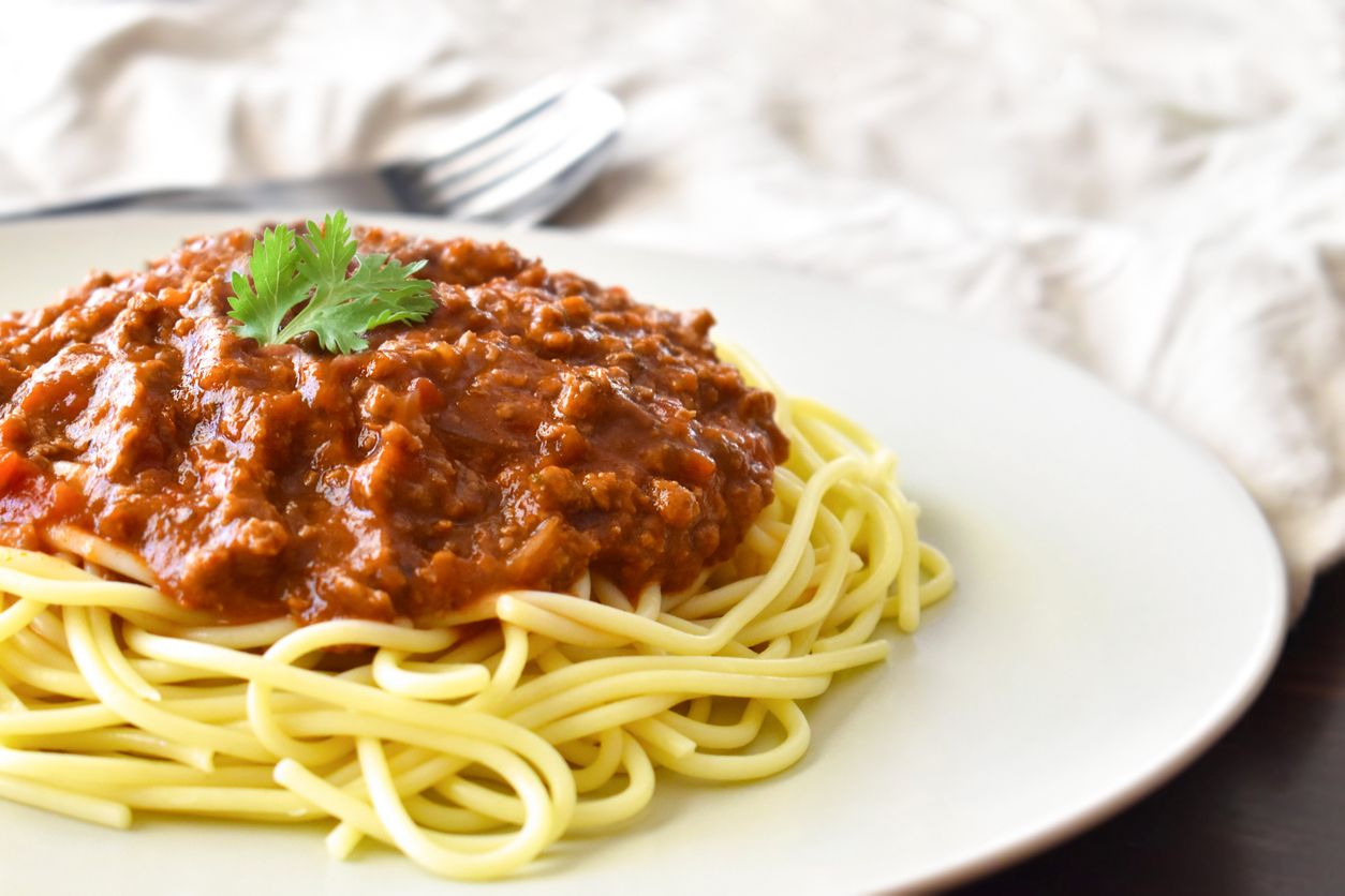 Spaghetti Bolognese with minced beef, onion, chopped tomato, garlic, olive oil, stock cube, tomato puree and Italian herb. Traditional Italian food on a  white plate.