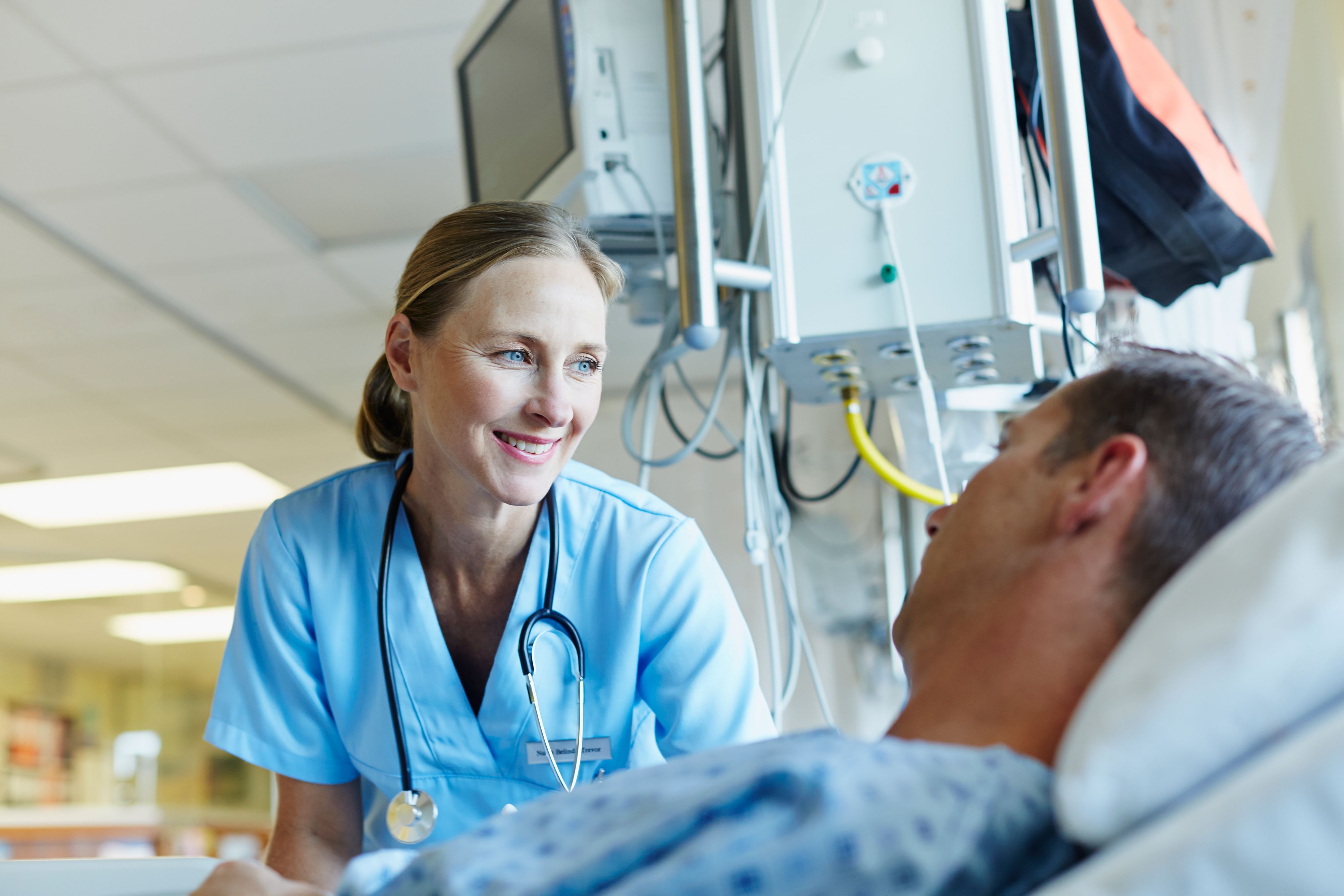 Happy female doctor looking at male patient lying in hospital ward