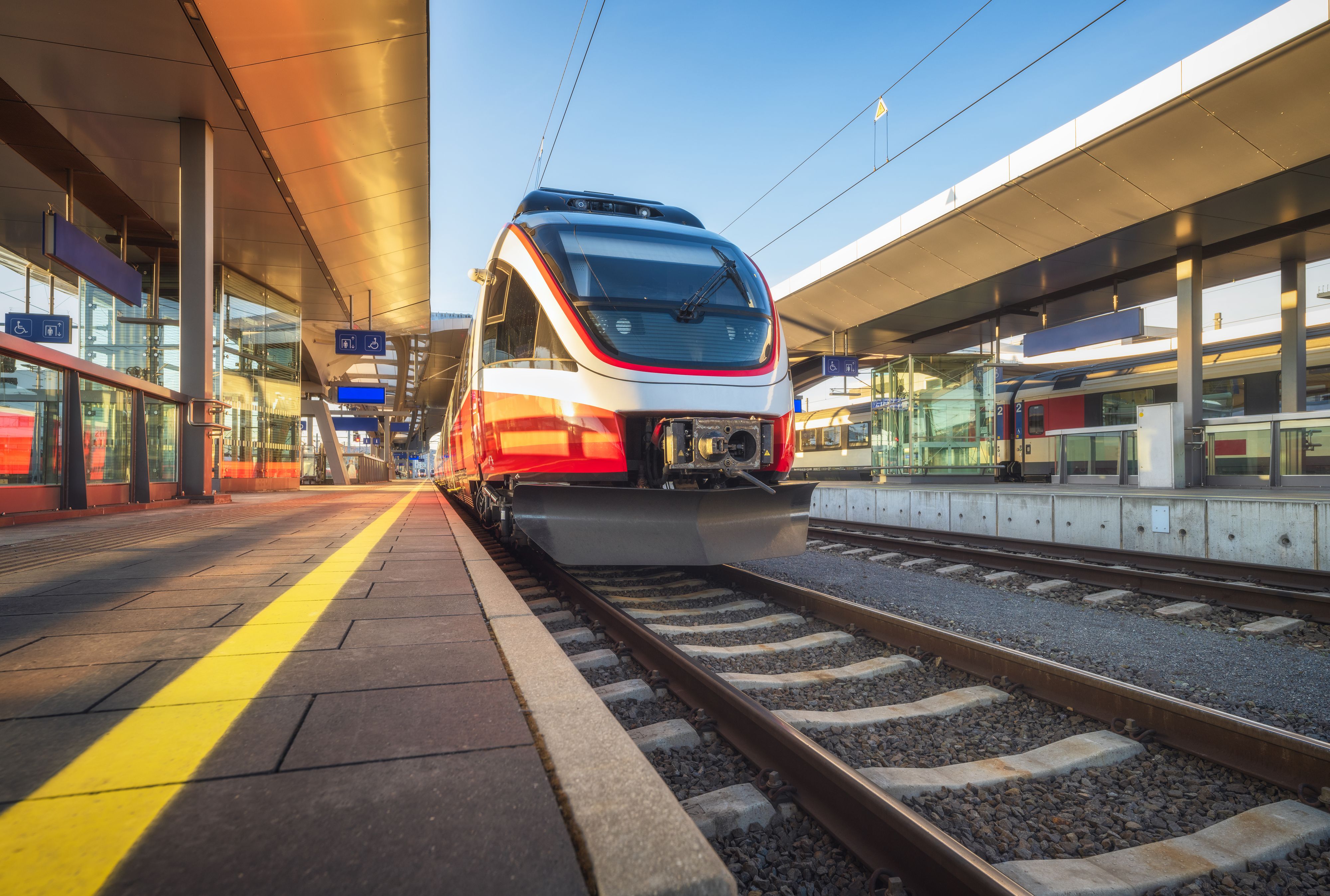 High speed train on the modern railway station at sunset in summer in Graz, Austria. Beautiful orange intercity passenger train on the railway platform. Railroad. Passenger railway transportation