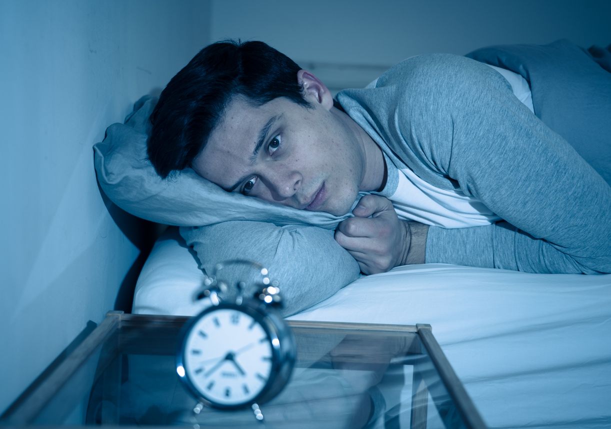 Sleepless and desperate young caucasian man awake at night not able to sleep, feeling frustrated and worried looking at clock suffering from insomnia in stress and sleep disorder concept.