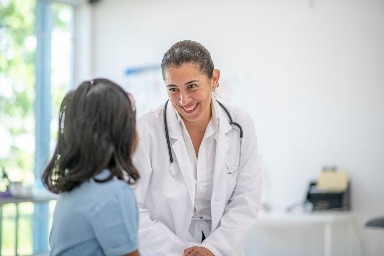 A girl of elementary age sits on the examination table while being seen by her doctor.