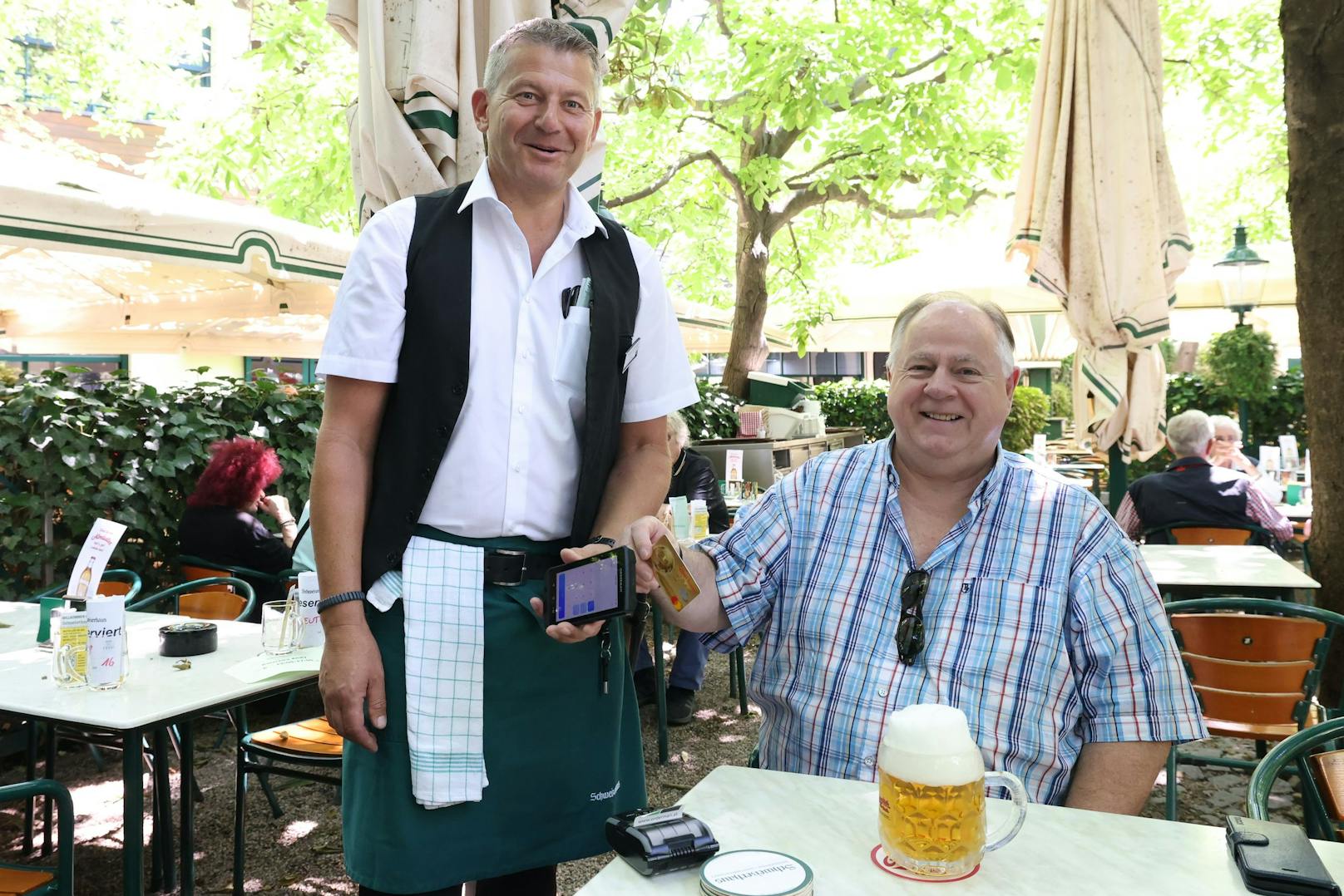 Kellner Heinz (li.) kassiert seit Saisonbeginn auch bargeldlos. Das Trinkgeld wählt Stammgast Toni direkt auf dem Bildschirm aus.