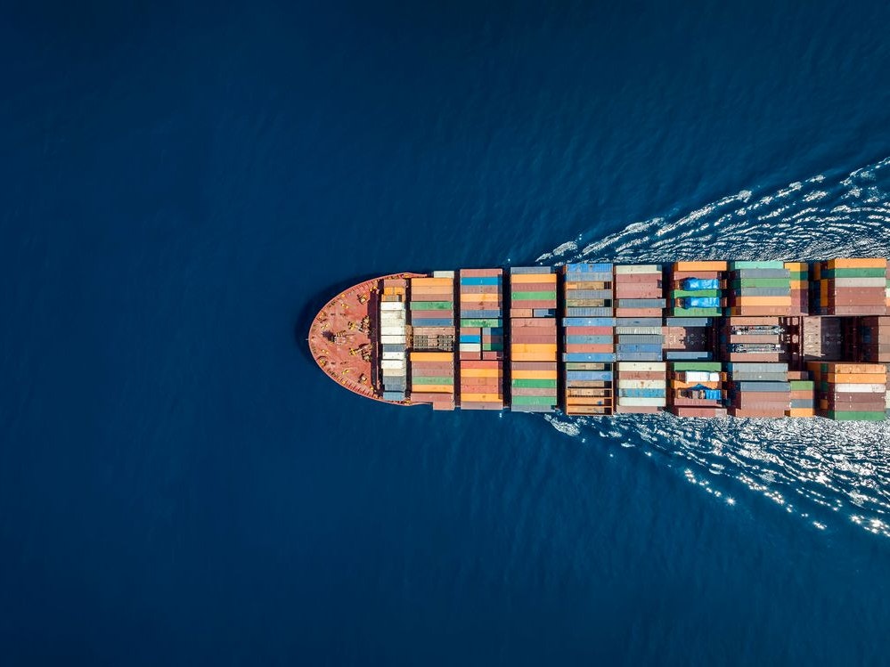 Aerial top down view of a large container cargo ship in motion over open ocean with copy space