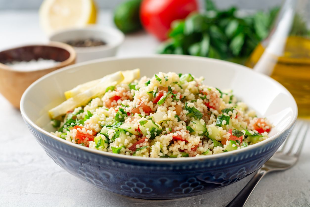 Traditional Arabic Salad Tabbouleh with couscous, vegetables and greens on concrete background. Selective focus.