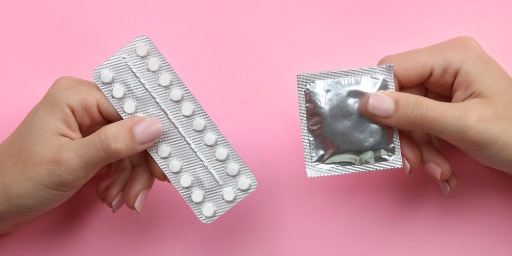 Contraceptive means: a condom and birth control pills in a hand on a pink background.