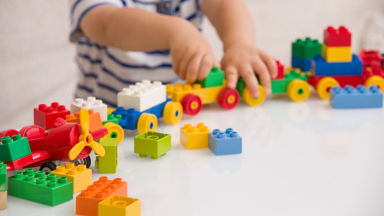 Close up of child's hands playing with colorful plastic bricks at the table. Toddler having fun and building out of bright constructor bricks. Early learning.  stripe background. Developing toys
