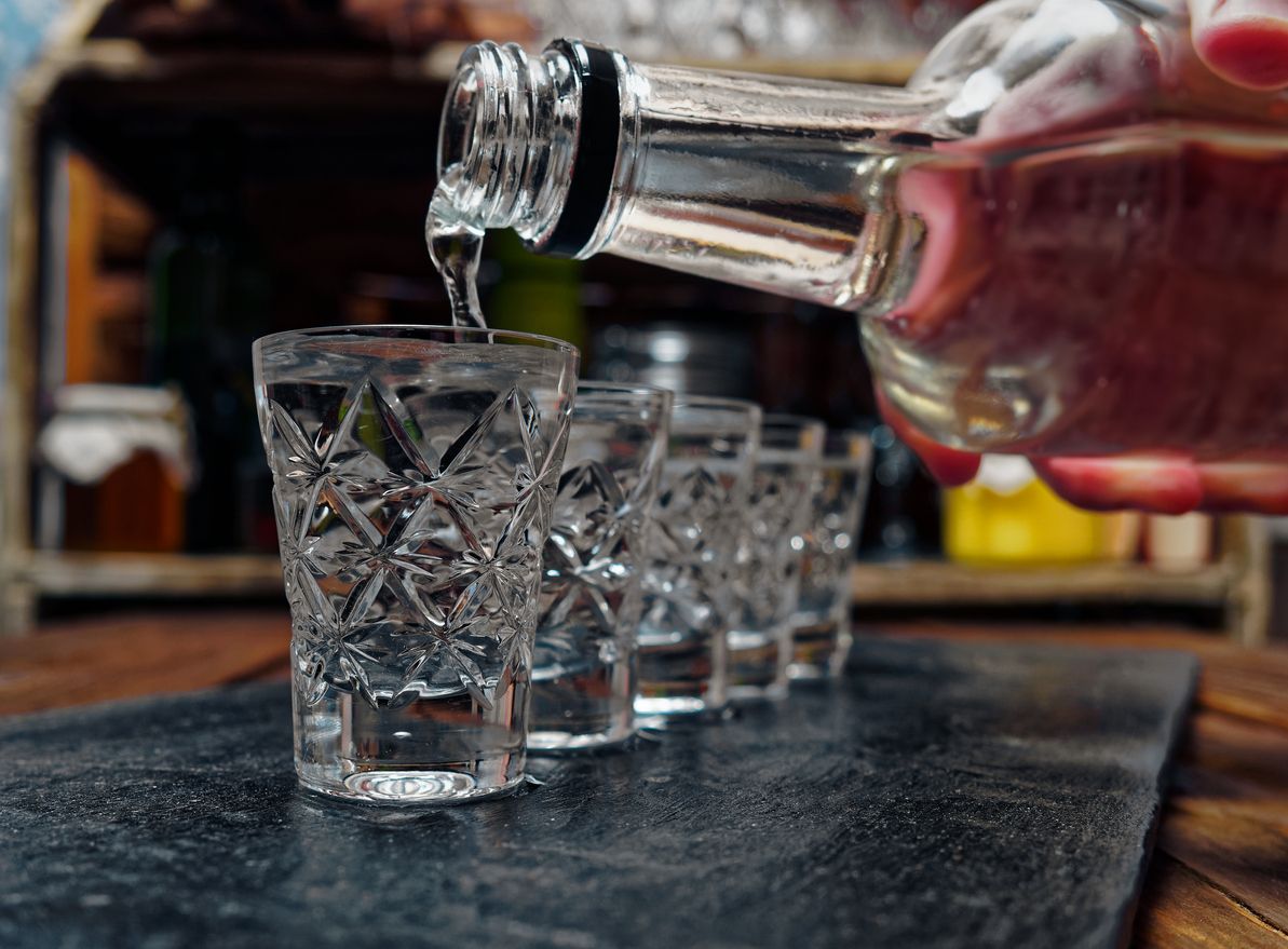 Crystal shot glasses of vodka standing in a row. Pouring vodka from a bottle to the shot glass