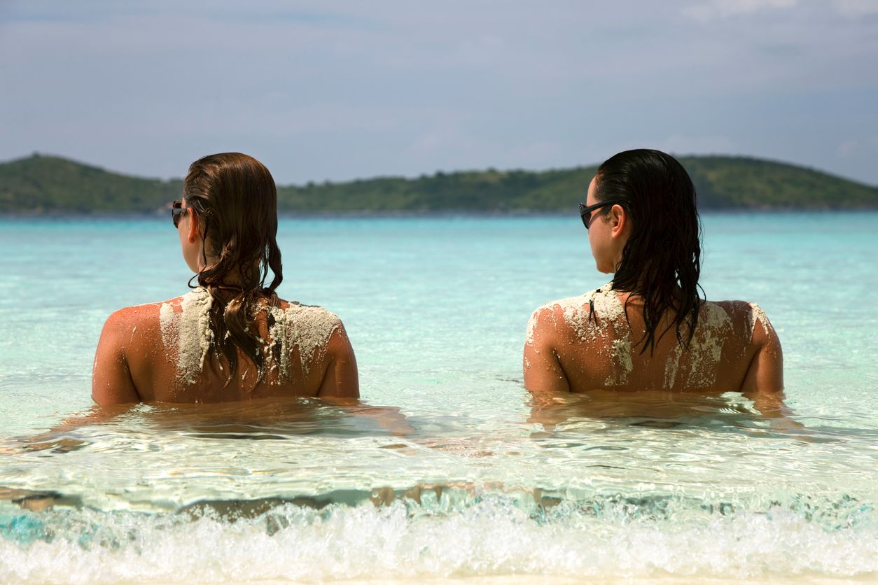 two topless women relaxing at the shoreline on a tropical beach