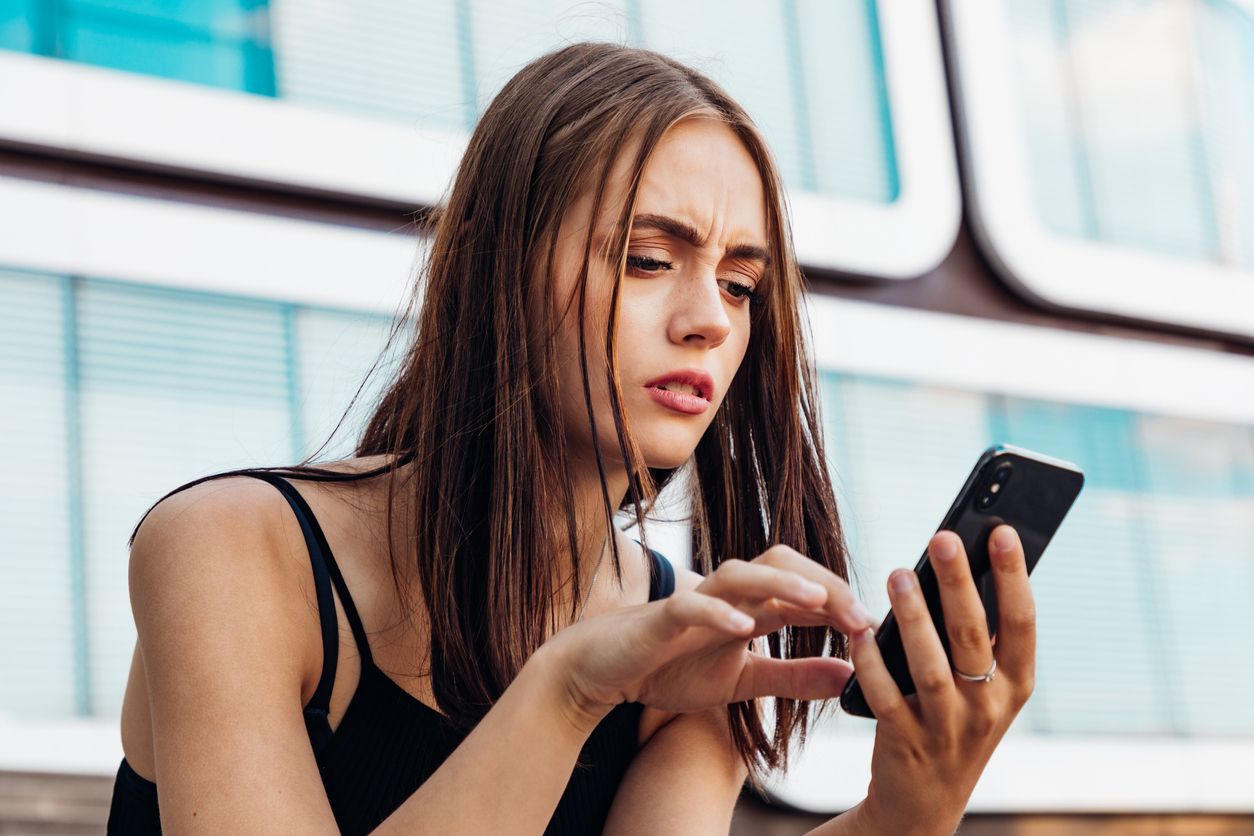 Reading Bad News on Mobile Phone. Young teenage woman checking her messages and social media post on her mobile phone. Looking worried and questioning reading the bad news and messages on her smart phone. Urban Young Generation Social Media Lifestyle Portrait.
