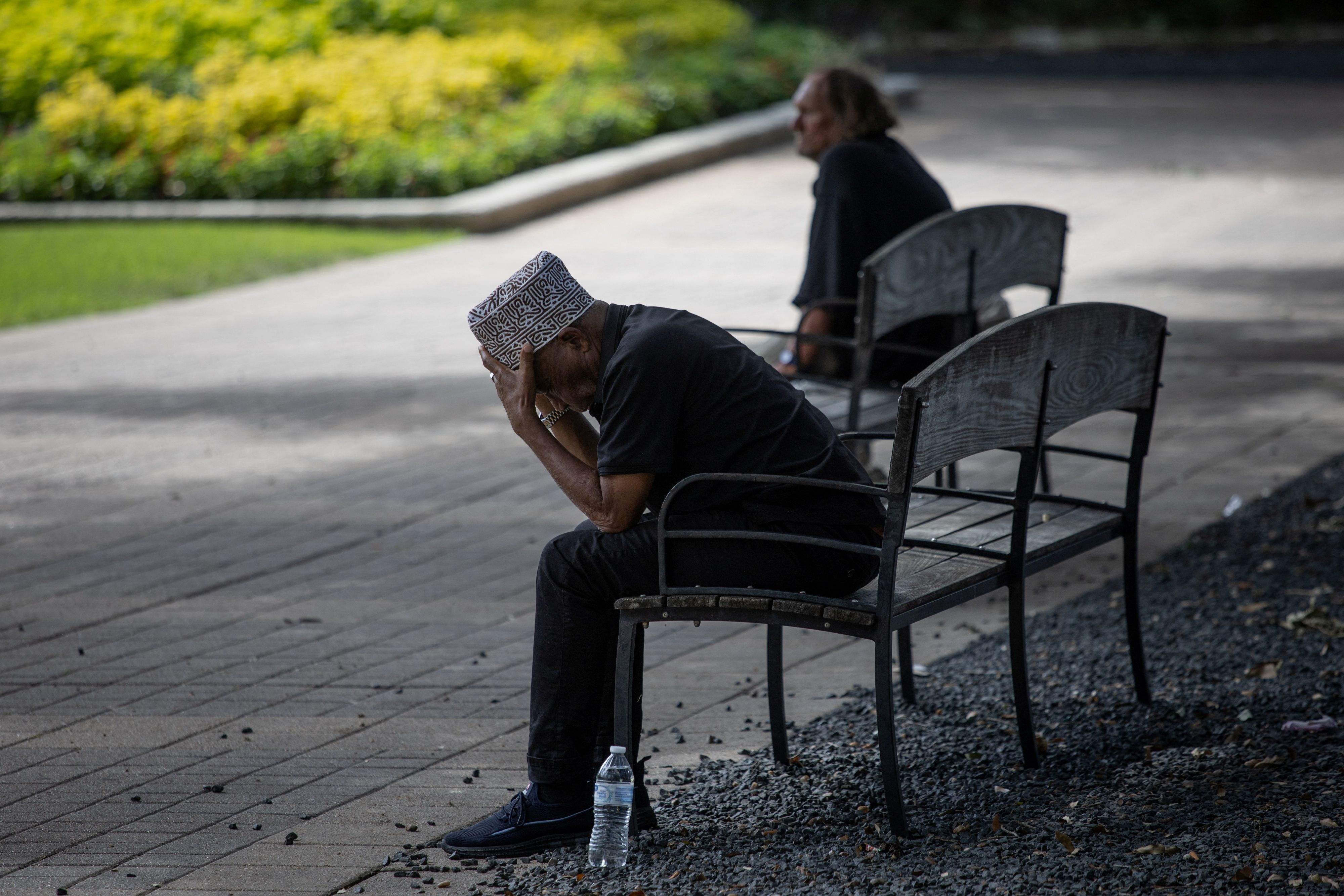 Men take cover on a city bench under trees during hot weather in downtown Houston, Texas, U.S., July 14, 2023.  REUTERS/Adrees Latif 