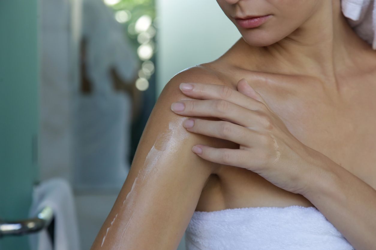 Woman applying body oil to moisturize her skin after shower, beauty skin care concept