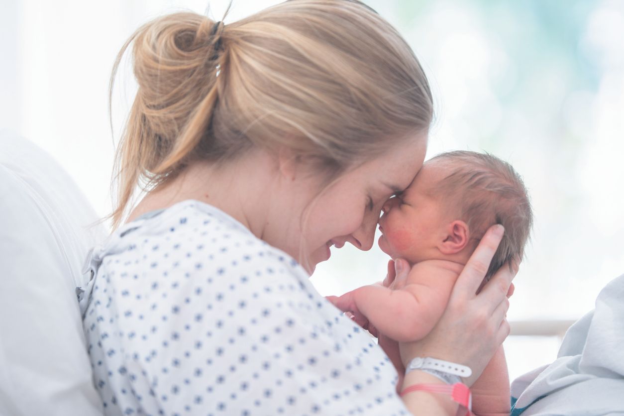 A mother is touching foreheads with her newborn daughter. They are laying in a hospital bed.