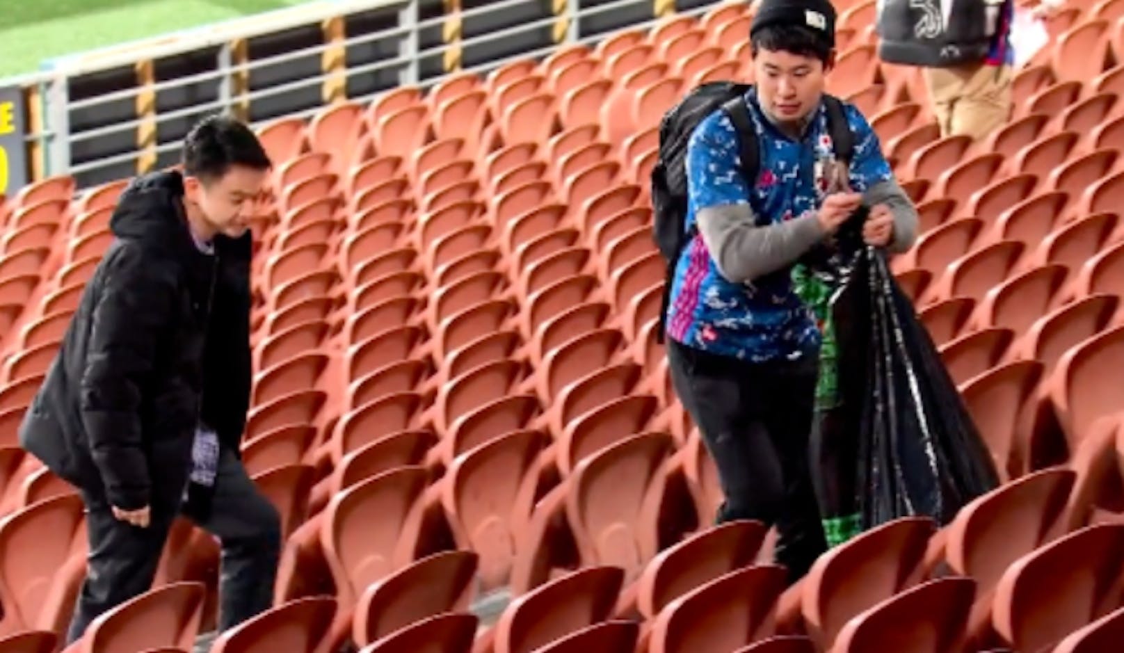 Die japanischen Fans sammeln mit Müllsäcken bewaffnet den Abfall auf der Tribüne ein.