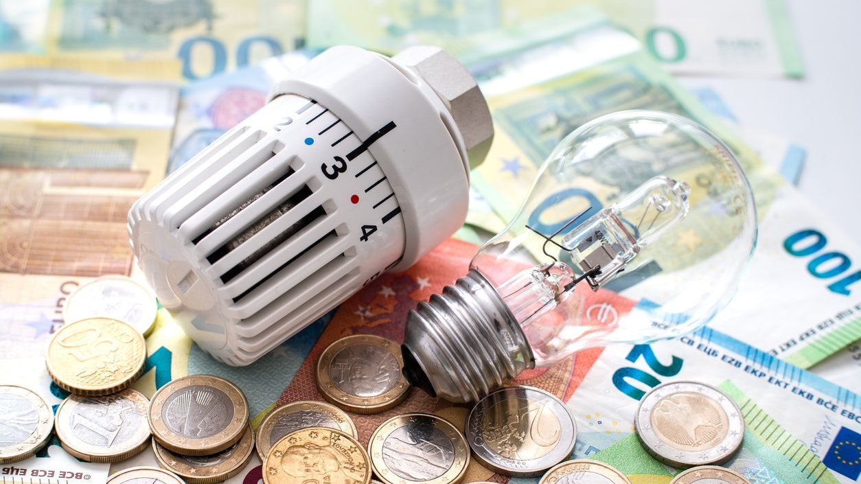 a heating valve and an old-fashioned lightbulb lie on top of euro bills and coins topic cost of energy supply