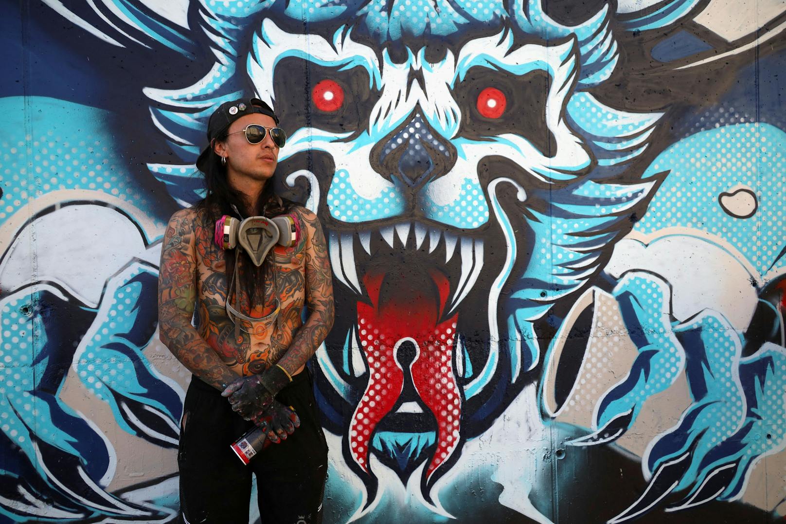 Julian Santamaria, ein Graffitikünstler aus Kolumbien, posiert mit seinem Wandbild im Rahmen des Graffiti-Festivals Meeting of Styles in Pristina.