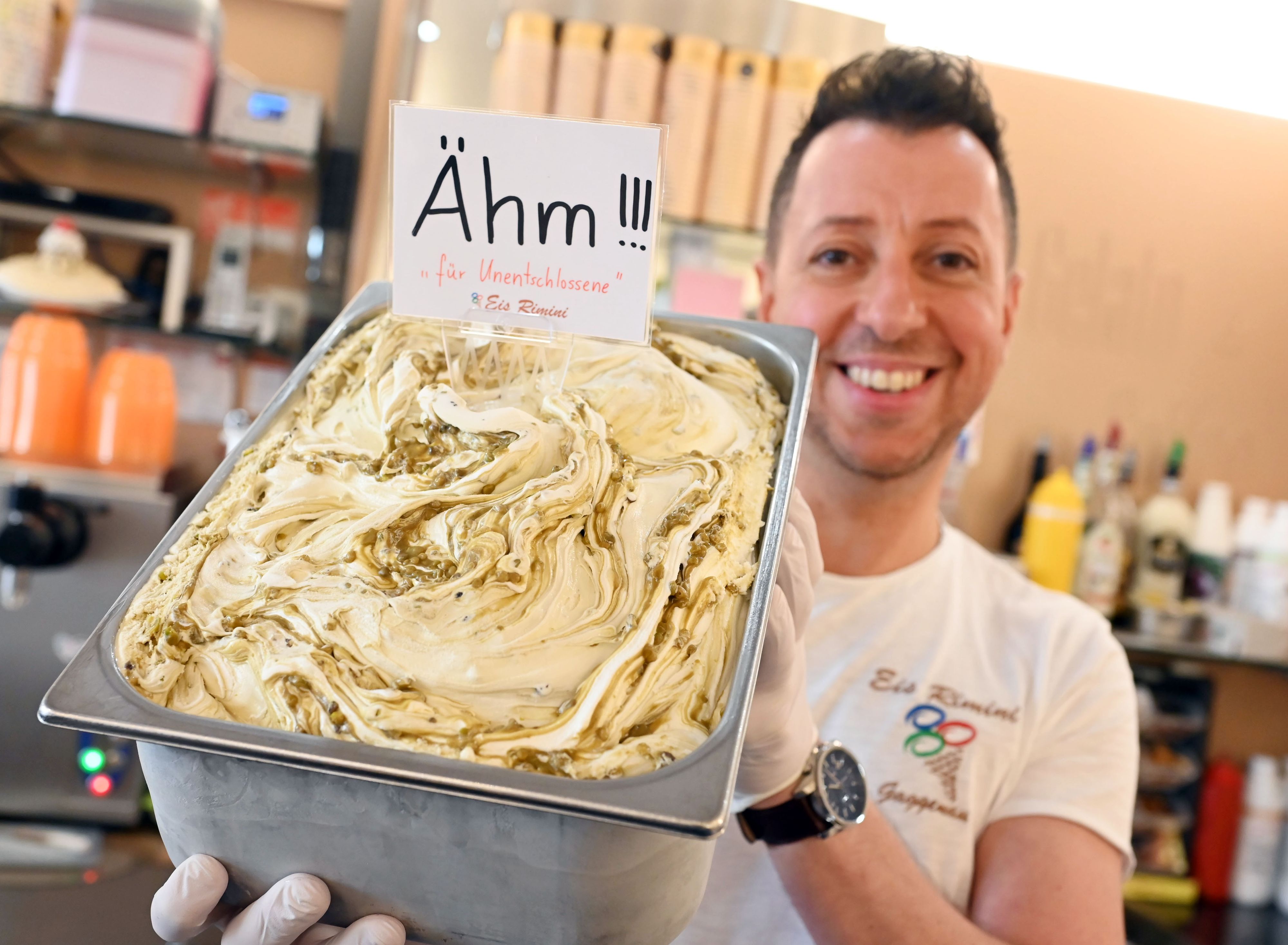 Download von www.picturedesk.com am 02.08.2023 (15:42).  PRODUCTION - 29 July 2023, Baden-Württemberg, Gaggenau: Alessandro Cimino shows off an "um" ice cream at his Rimini ice cream parlor. If you don't know exactly what you want and start your order with "um" at the ice cream parlor, you can get an "um" ice cream in a cone or cup. It is a milk ice cream creation made of white chocolate mixed with pistachio crunch. Photo: Uli Deck/dpa - 20230729_PD17546 - Rechteinfo: Rights Managed (RM)