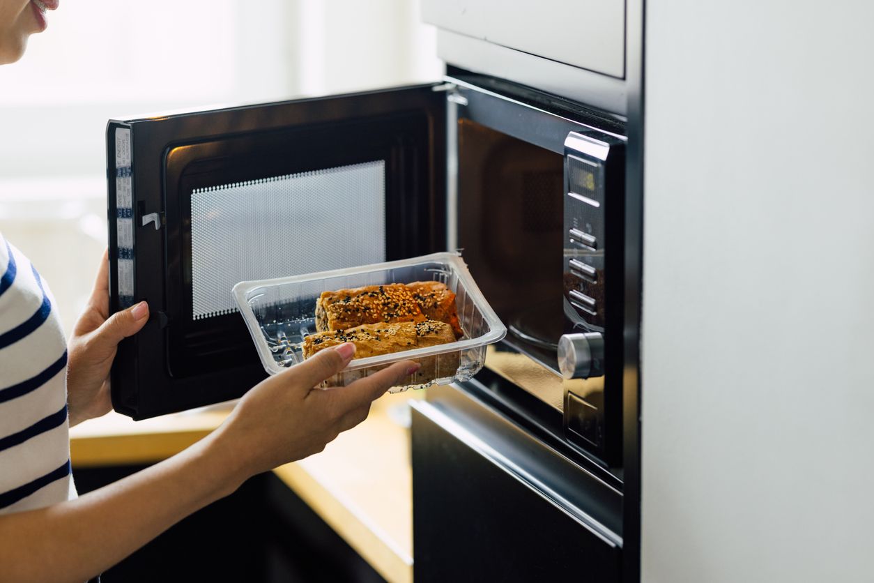 An unrecognizable woman reheating a meal in a microwave oven.