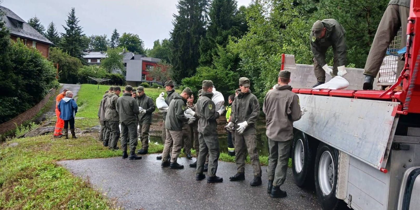 Soldaten stabilisieren einen hochwassergefährdeten Damm zusammen mit örtlichen Hilfskräften mit Sandsäcken.