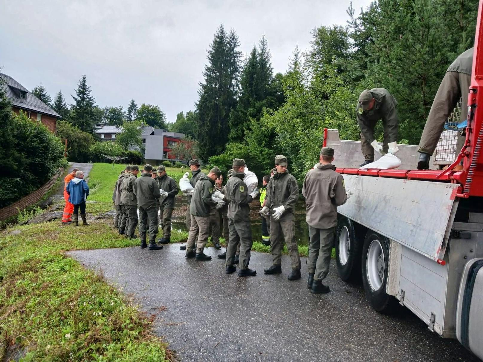 Soldaten stabilisieren einen hochwassergefährdeten Damm zusammen mit örtlichen Hilfskräften mit Sandsäcken.